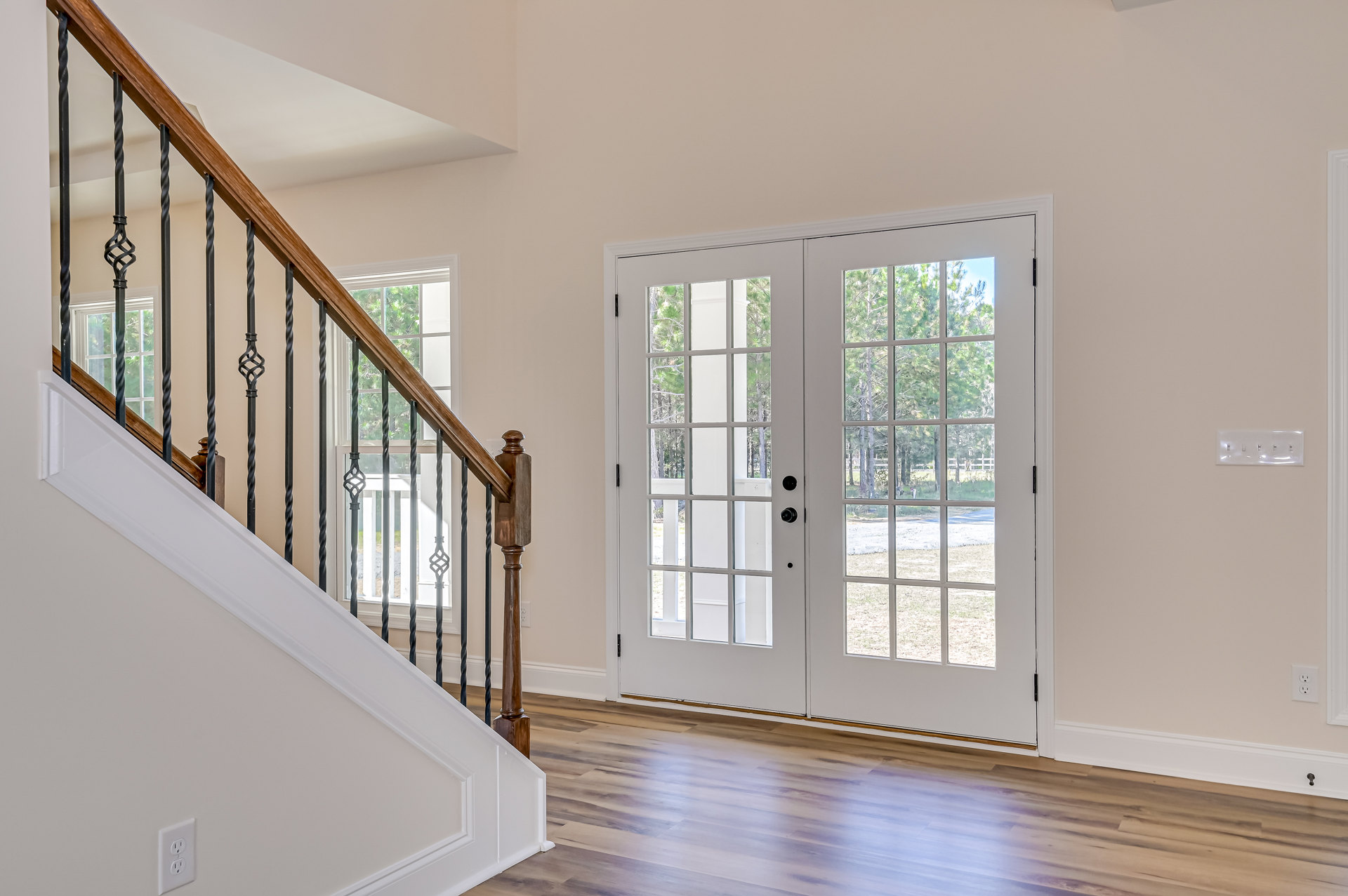 Wood staircase with black metal railings leading to white double doors with glass panes, light switch and electrical outlet visible on adjacent wall, hardwood flooring throughout