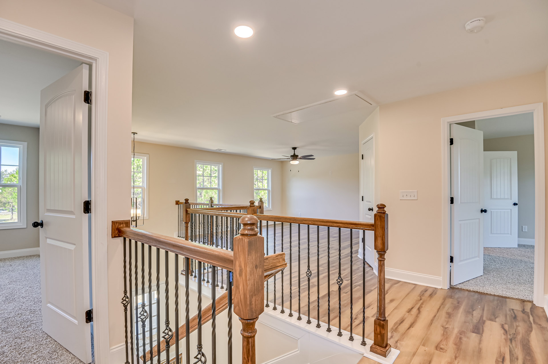 Wood staircase with white balusters and handrail, white ceiling featuring recessed light and smoke detector, window showing green trees outside, white door with black knobs