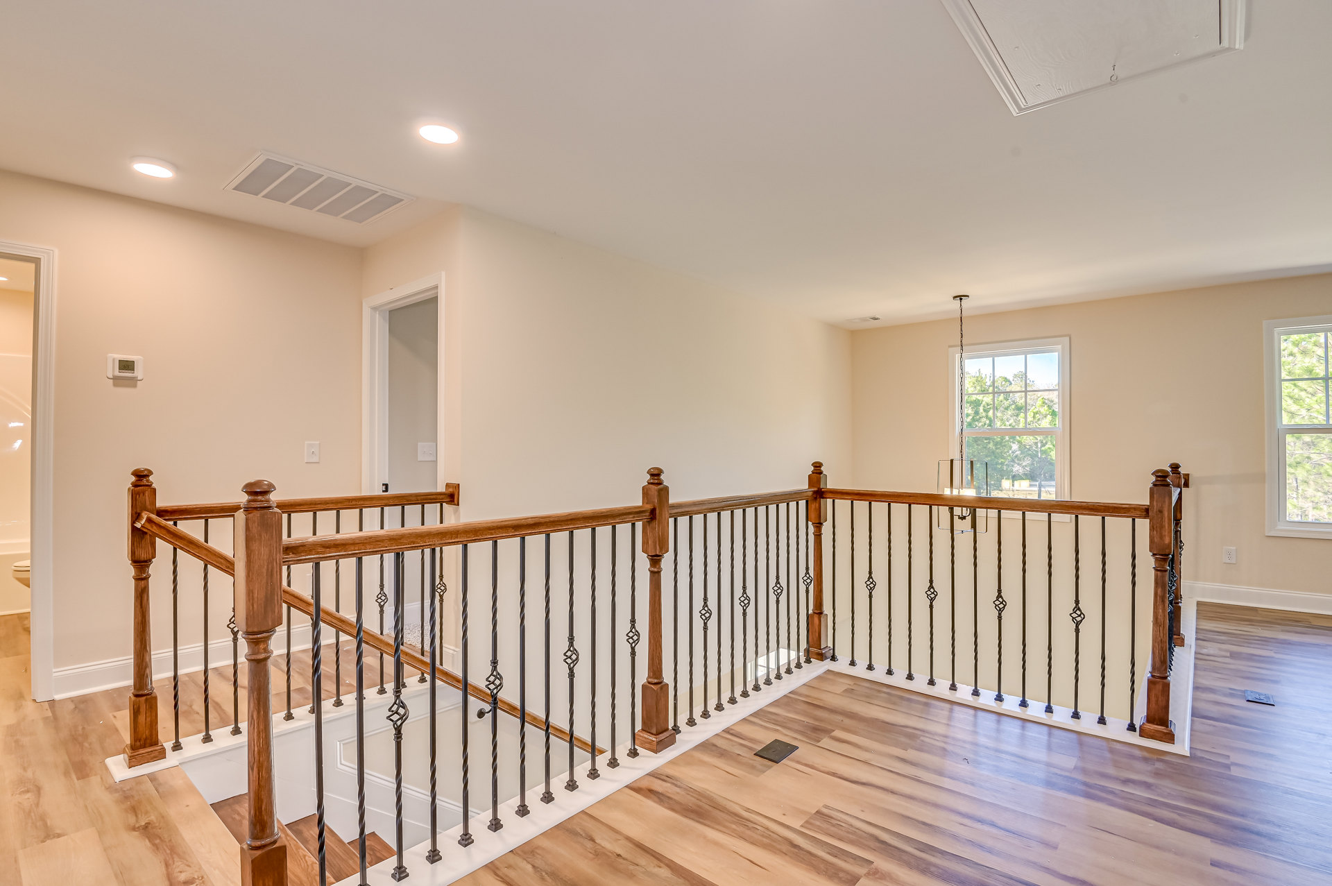 Wood and metal staircase with laminate flooring, large window showing tree outside, wooden post supporting metal railing, white walls, chain hanging from window frame