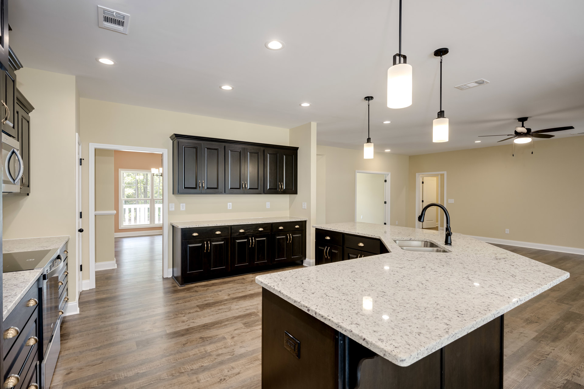 Spacious kitchen featuring a large central island, black cabinets with gold handles, white countertops, built-in sink with modern faucet, wall-mounted vent, and pendant lighting