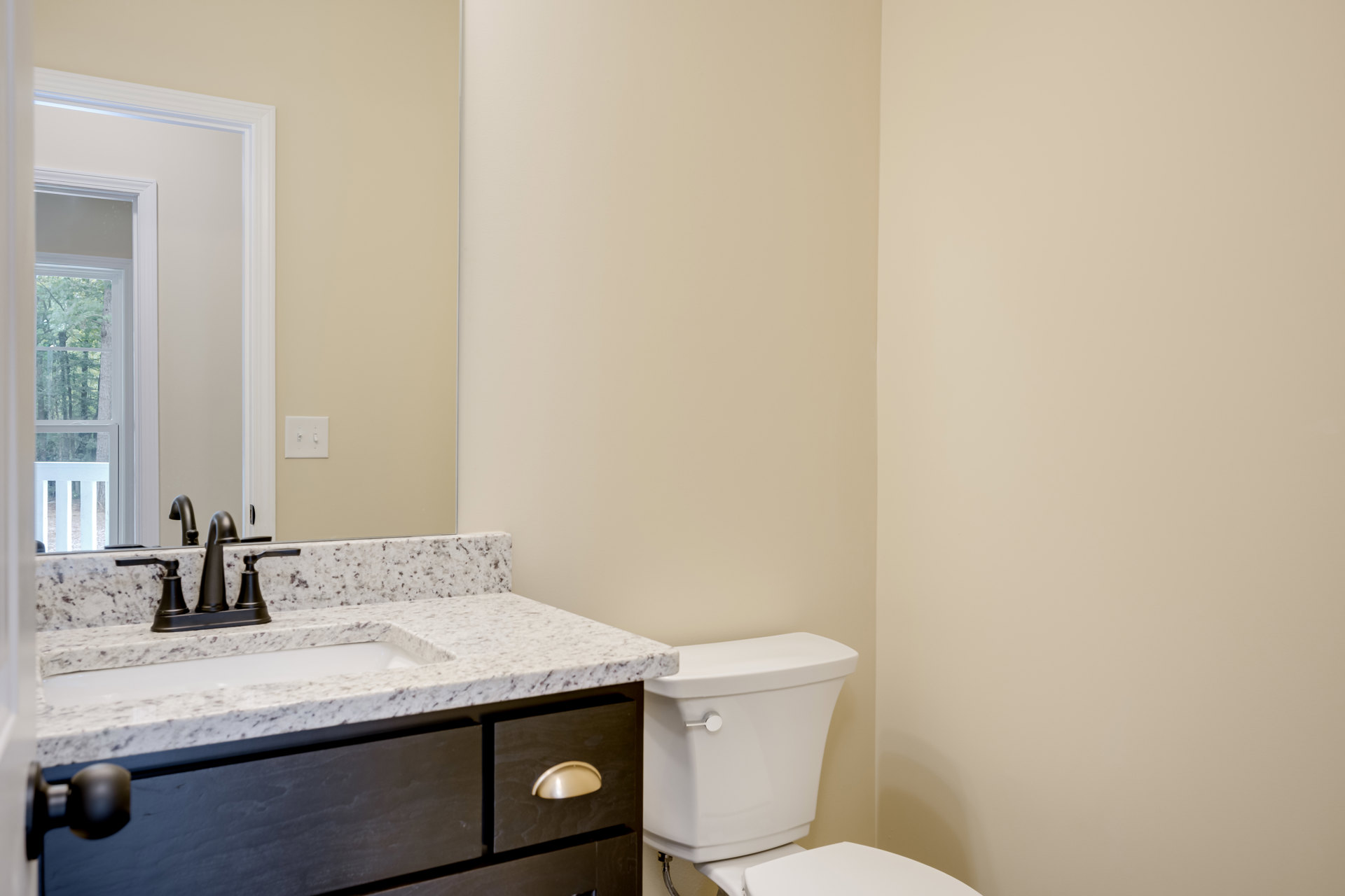 White bathroom with tile floor, modern sink and drawers, white toilet, wall-mounted light switch, close-up lamp, white door with window showing trees outside