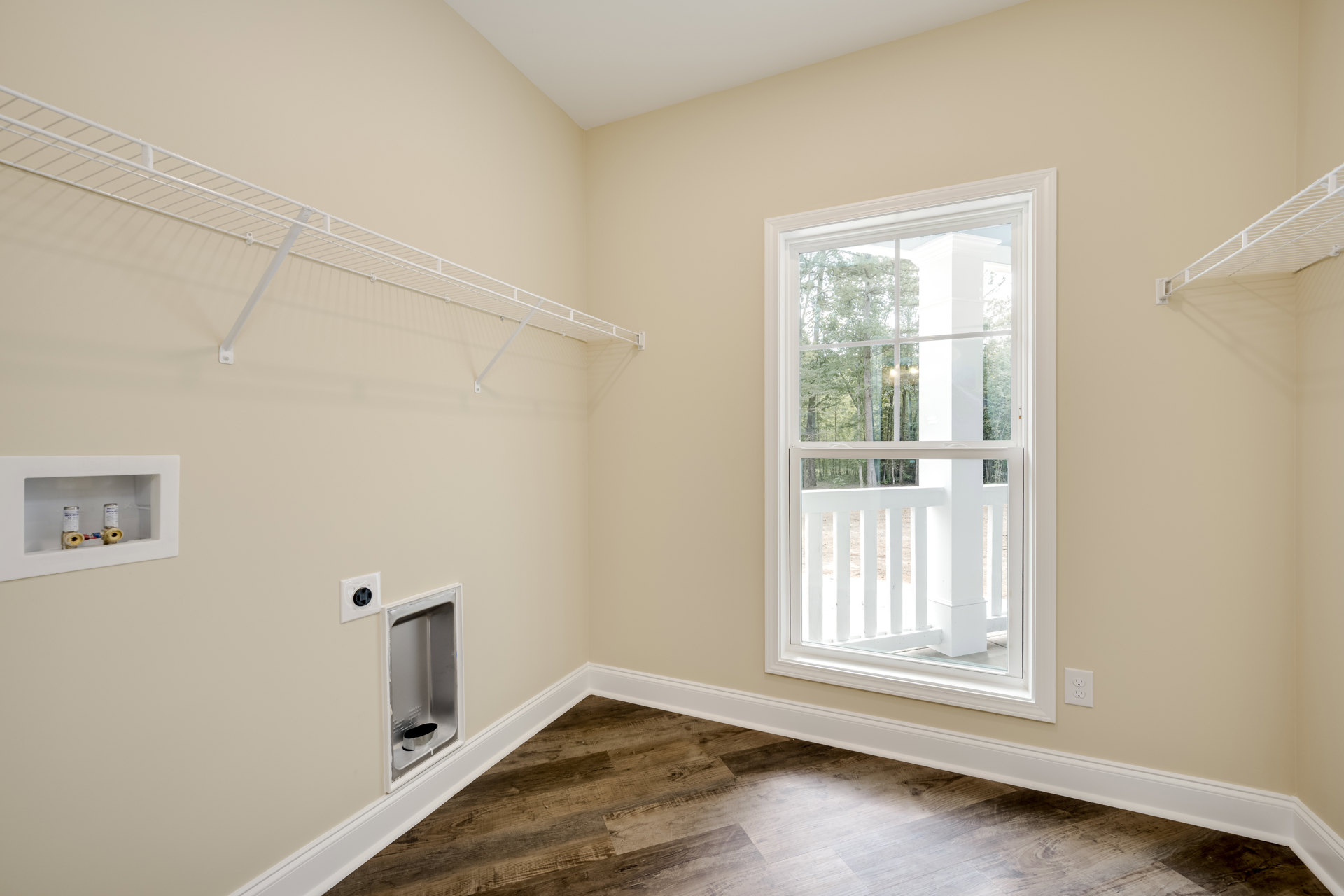 Sunlit room featuring a large window with a white frame and railing, wood flooring with white trim, and a white wall-mounted shelf.