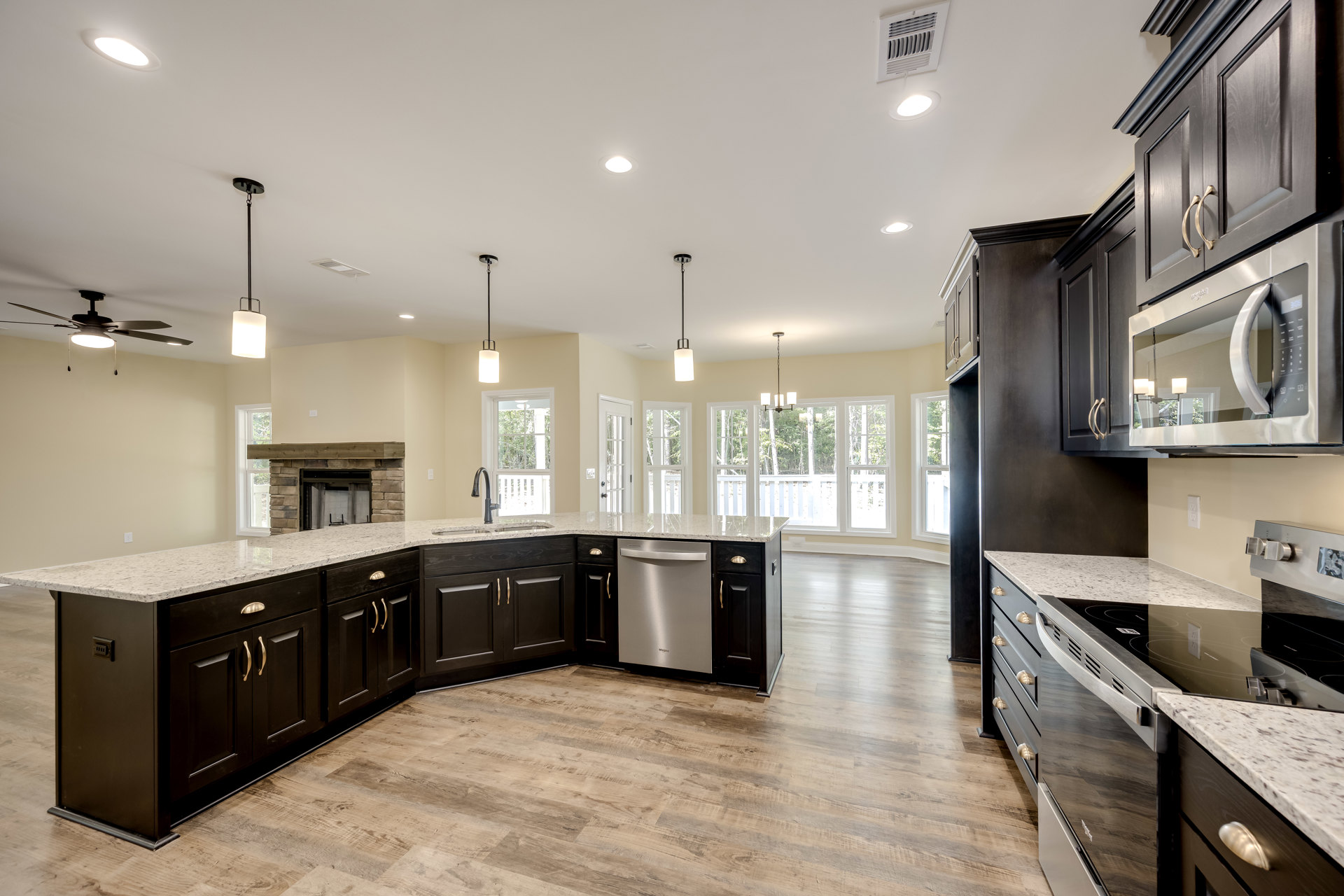 Open kitchen with white cabinetry, stainless steel stove and dishwasher, large central island, built-in microwave, stone fireplace, and light wood flooring