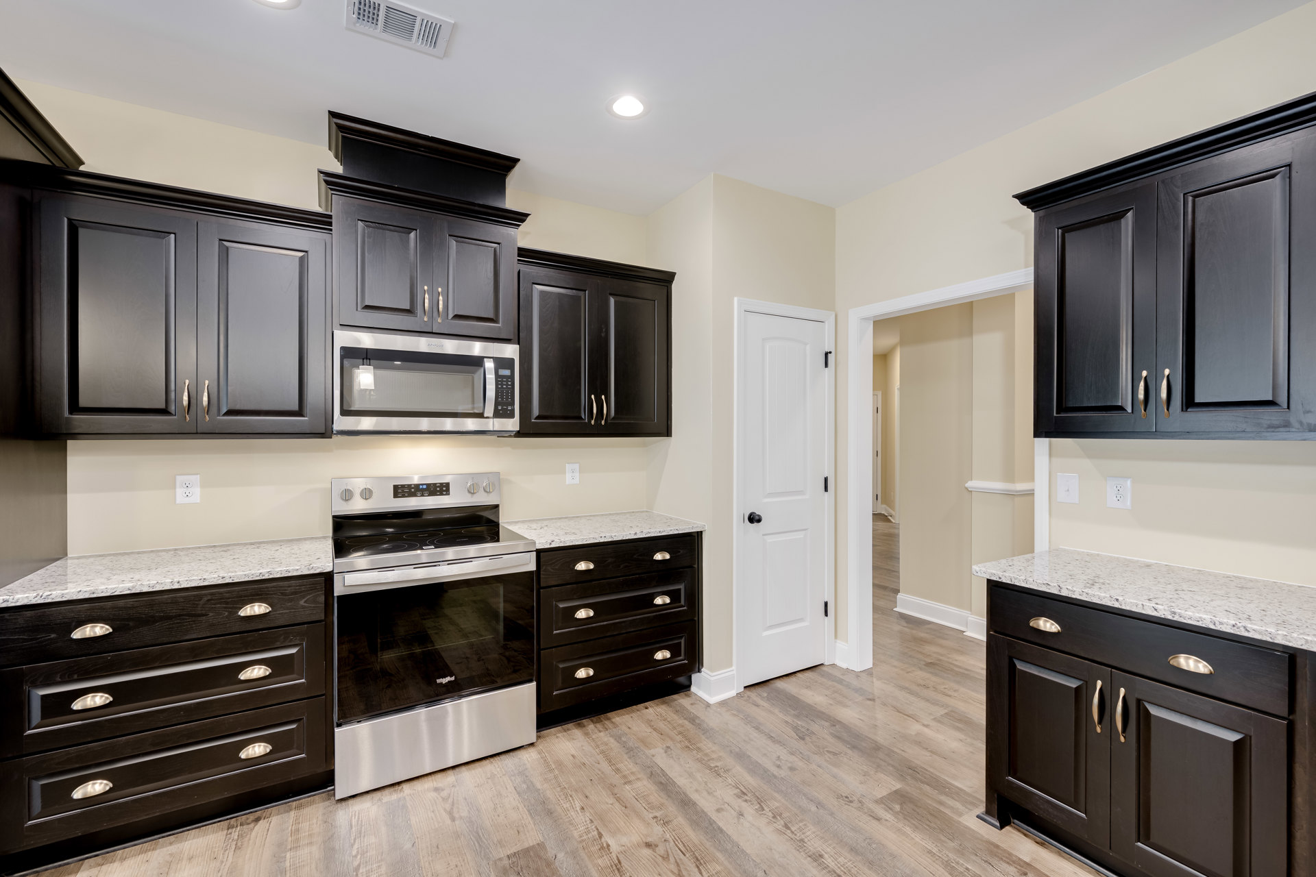 Black kitchen cabinets with silver handles, white countertops, stainless steel stove with glass door, built-in microwave, and drawers, set against light walls.