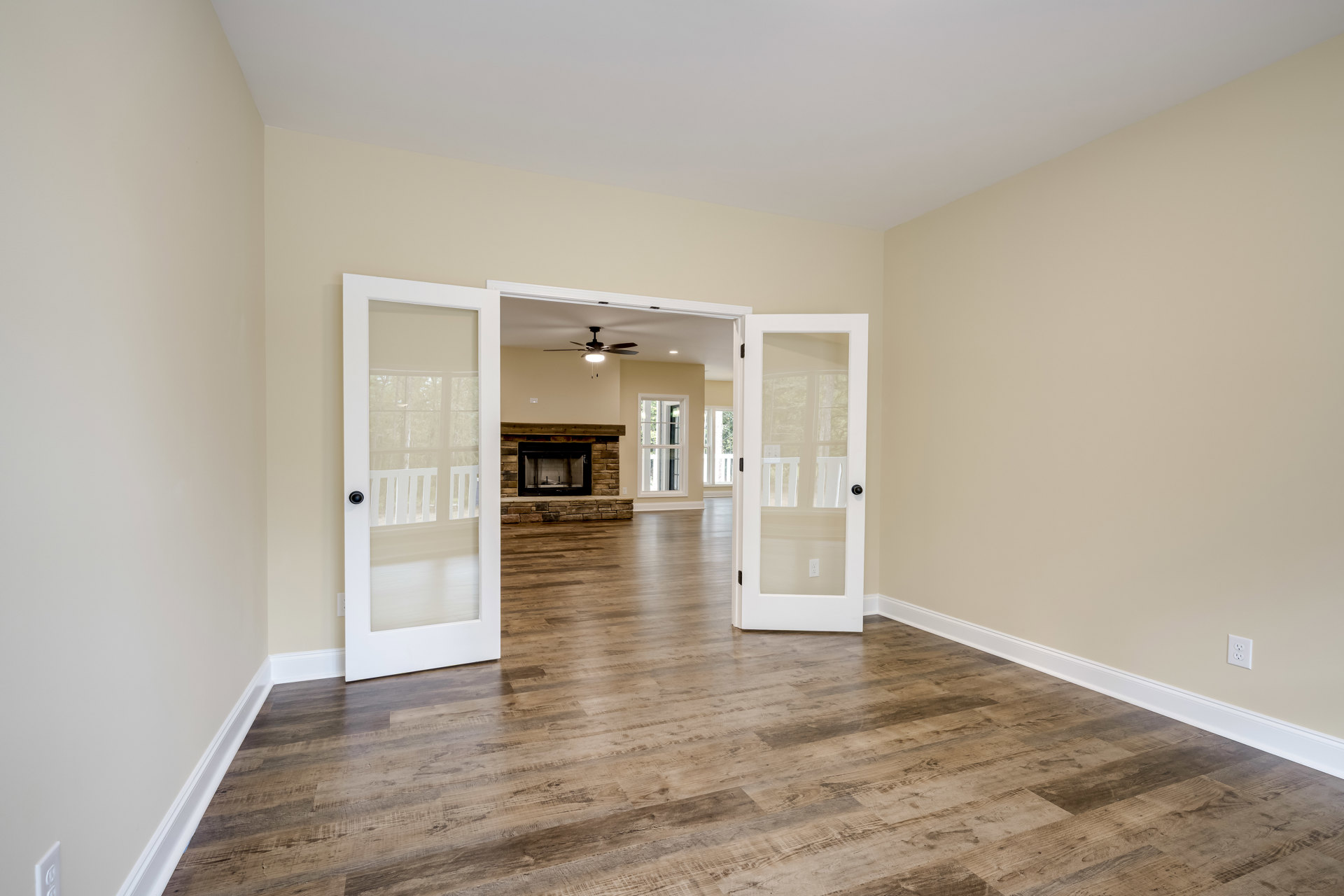 Living room with wood flooring, white plaster walls, glass-paneled door with black handle, and central fireplace featuring a white surround and metal screen.