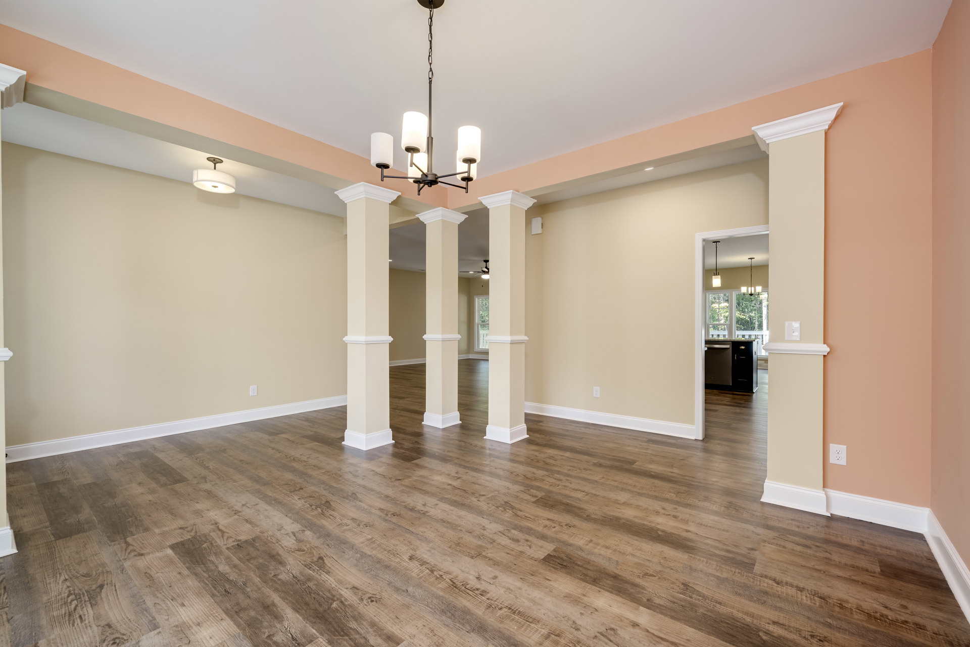 Open living area with polished wood flooring, white columns, granite kitchen countertop, and modern chandelier with white lights