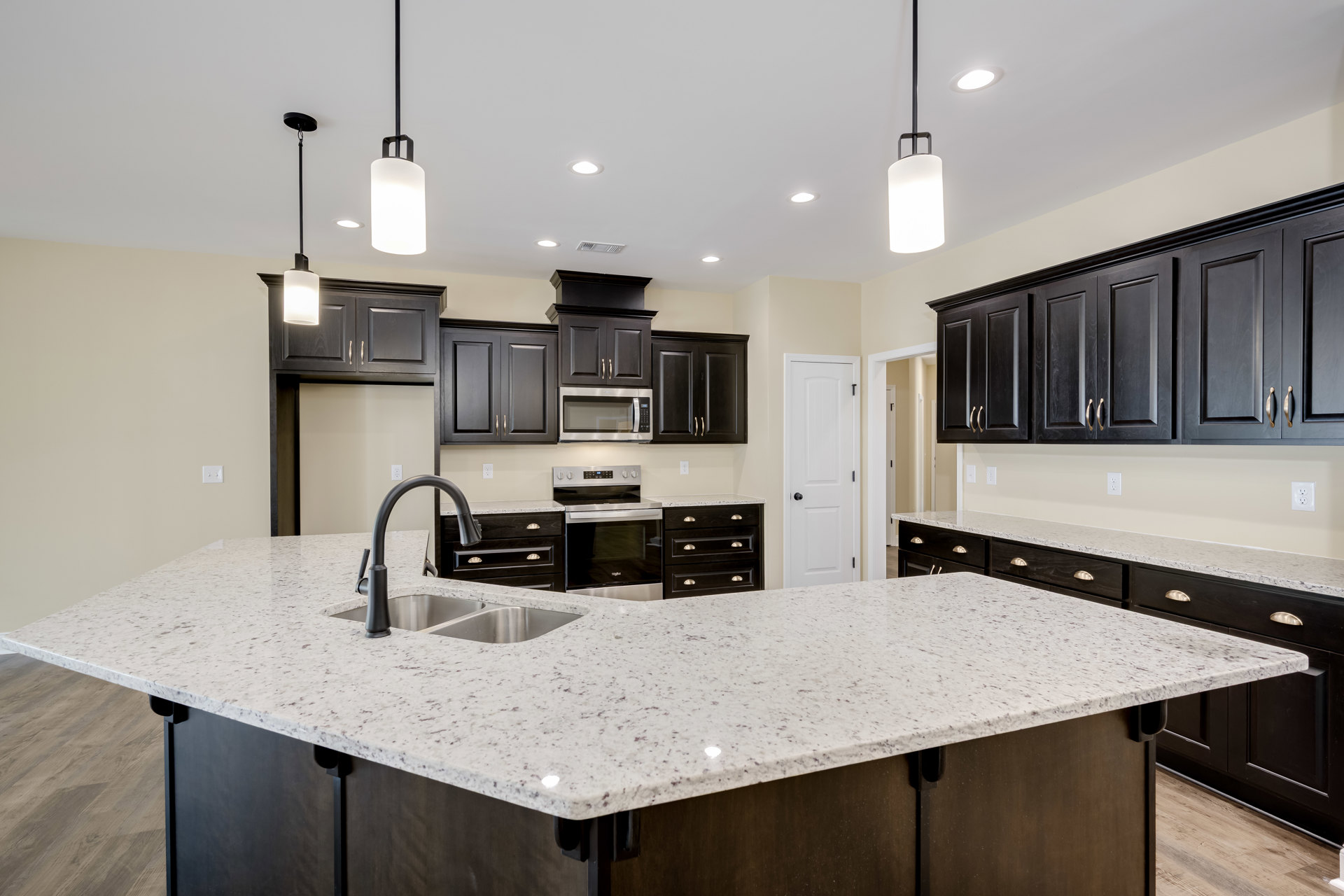 Spacious kitchen featuring a large white island with granite countertop, black cabinets, stainless steel sink, built-in microwave, and modern appliances.