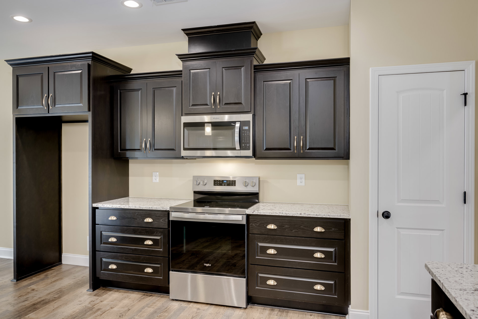 Black kitchen cabinets with silver handles, stainless steel oven with glass door, built-in microwave, white door with black knob, black framed board on wall, light countertops