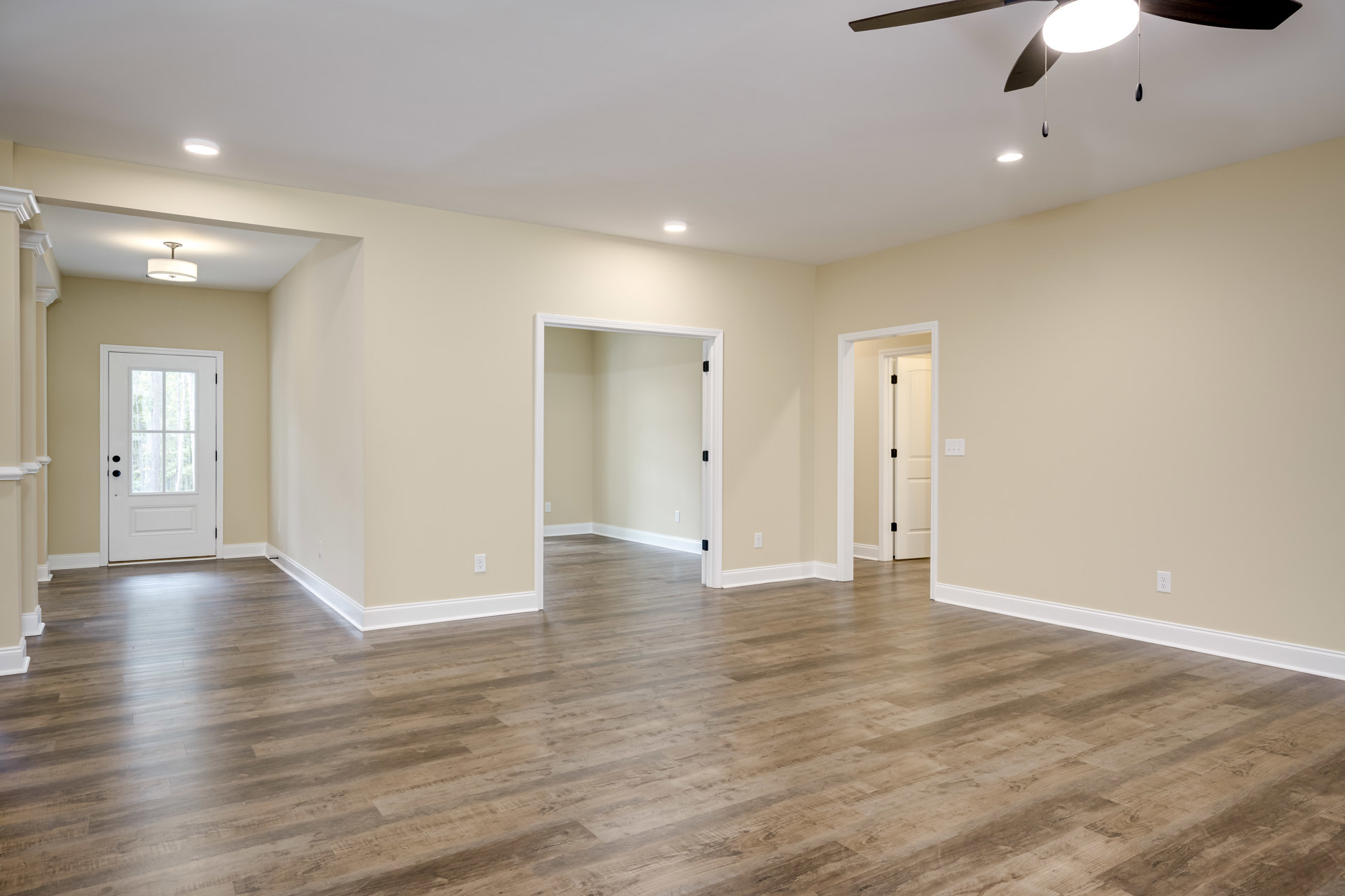 Wood flooring with white baseboards, ceiling fan with chain, open white door featuring glass panes, white walls, and a small surface with black dots.