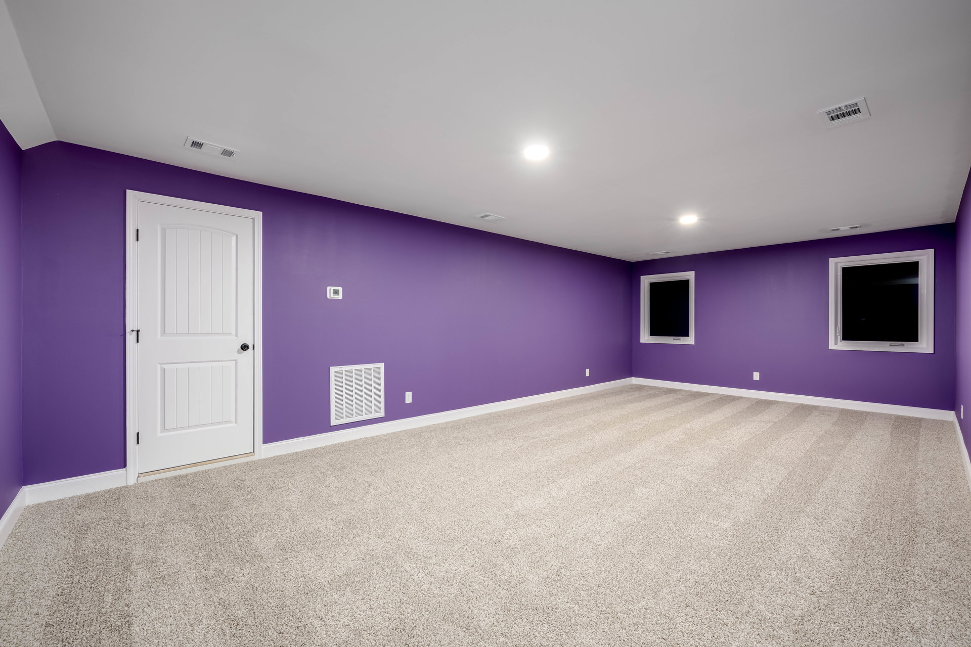 Purple walls and carpeted floor, white window frame with black screen, white door with black handle, white vent on wall