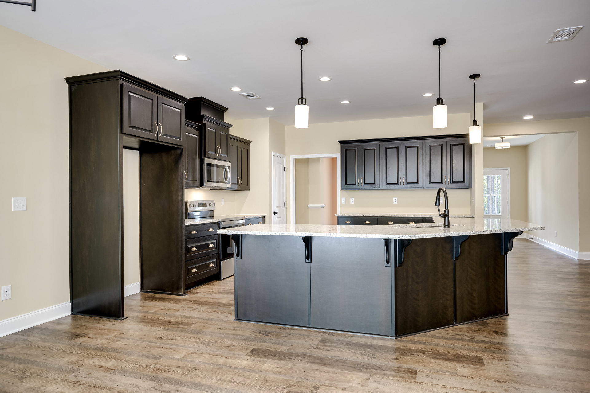 Spacious kitchen featuring a large marble island, white cabinetry, stainless steel stove, modern pendant lighting, and hardwood flooring
