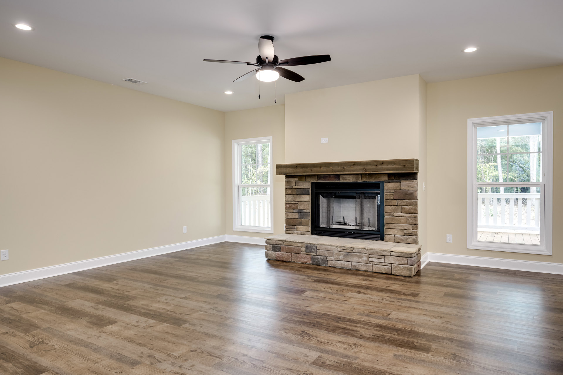 Living room with wood mantle fireplace, mesh screen, ceiling fan with light, large window overlooking porch and trees, neutral walls and flooring