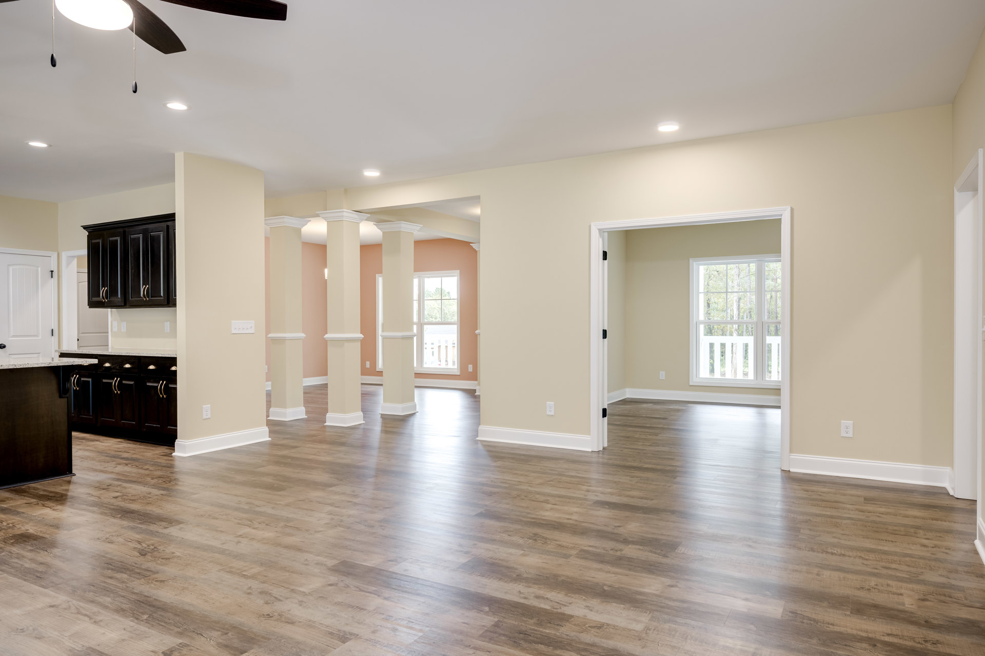 Spacious kitchen with white columns, wood flooring, black cabinets with gold handles, white walls, and large window framed in white overlooking trees