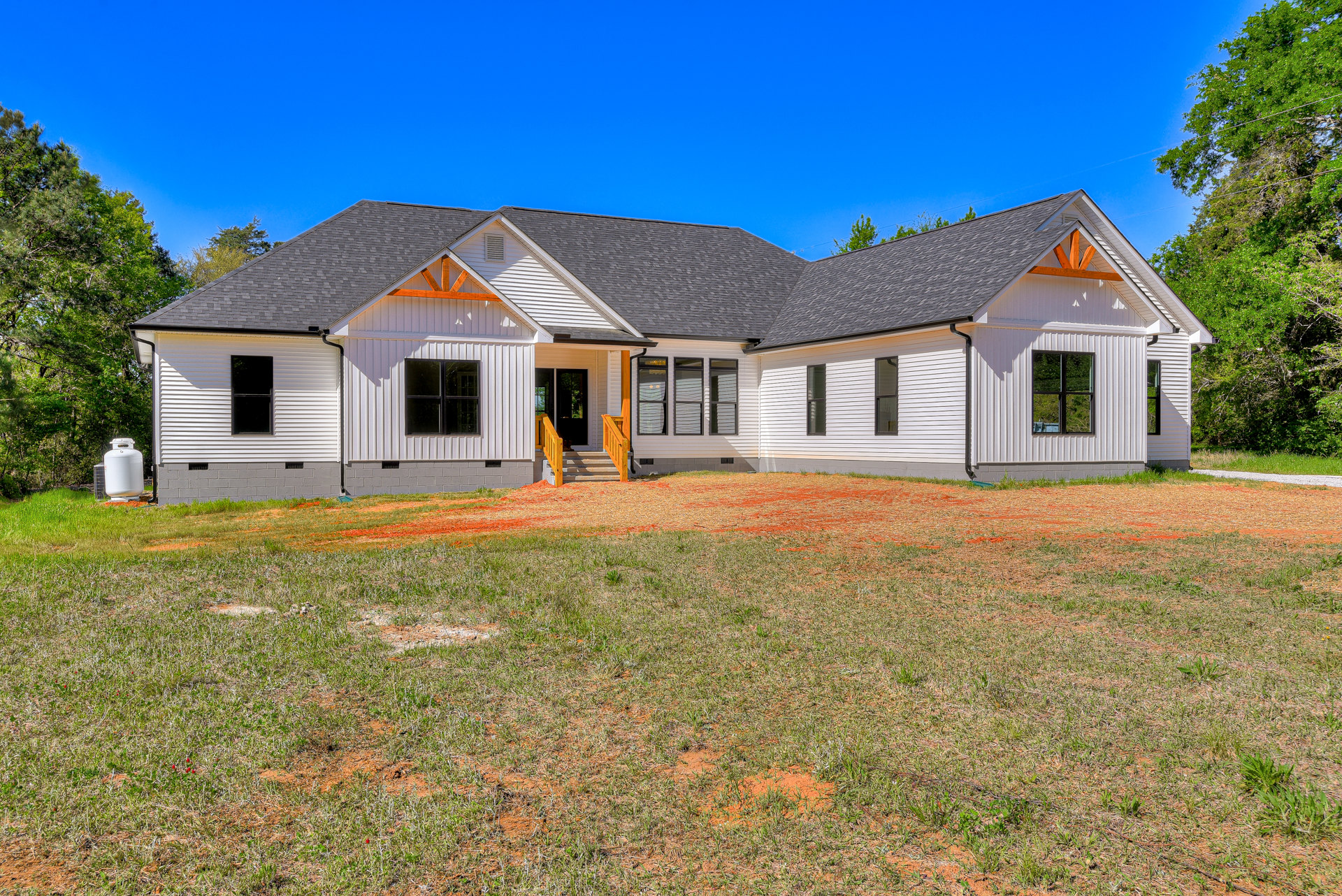 White two-story house with large windows, front porch and stairs, manicured green lawn, wooden railing, and a cat sitting near the entrance.