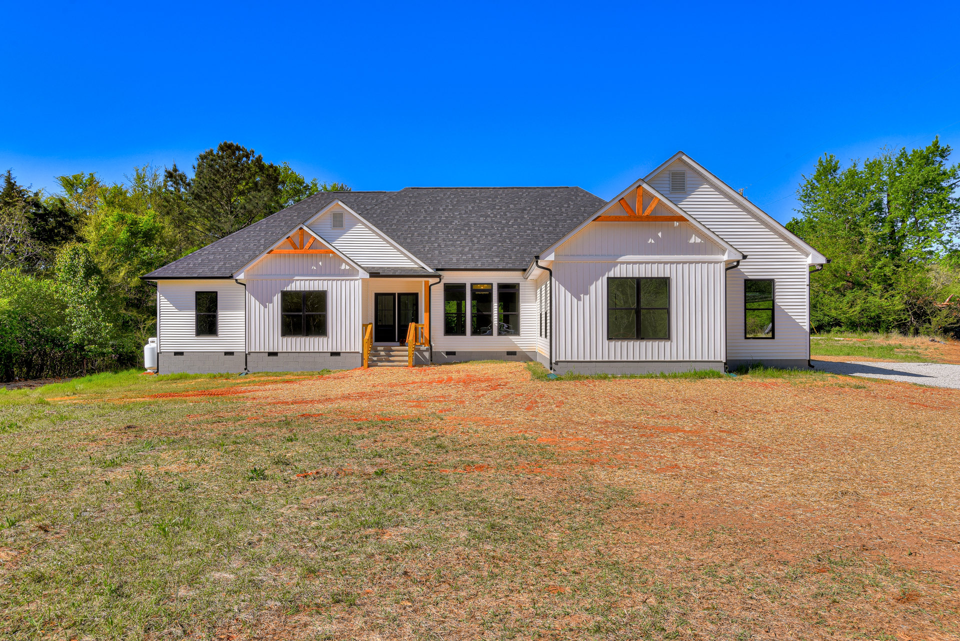 White cottage-style home with black roof, surrounded by green lawn and mature trees, Robert Frost Farm visible in the background, clear blue sky overhead, multiple windows and