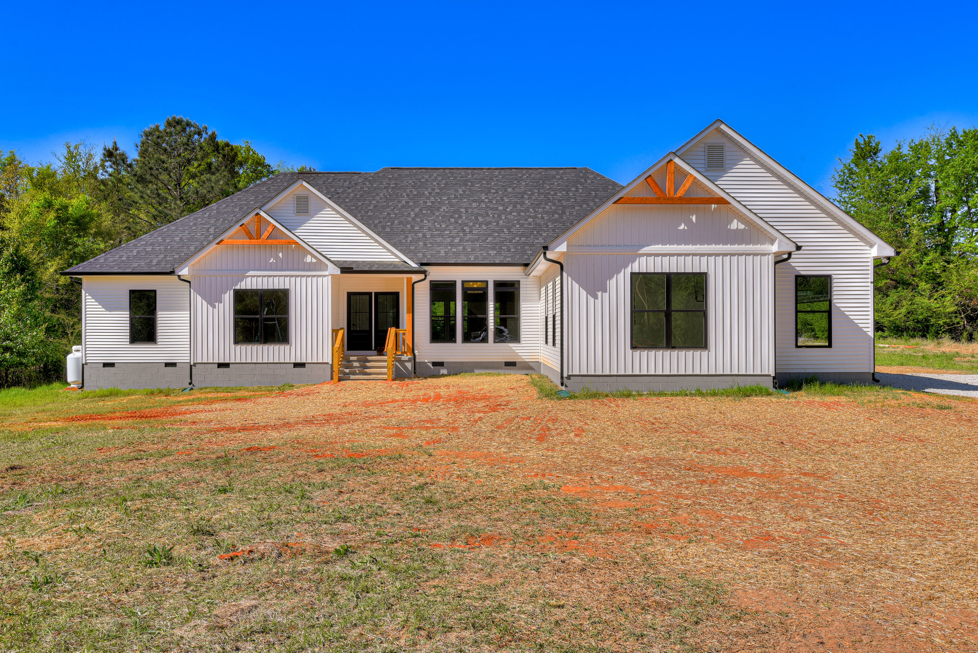 Two-story cottage-style home with white siding, front porch and stairs, surrounded by green grass yard, wooden railing, mature trees, and blue sky with scattered clouds; Robert