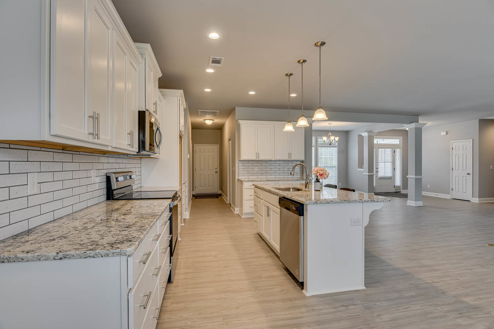 Kitchen with white shaker cabinets, granite countertops, stainless steel dishwasher in the island, tile flooring, recessed ceiling light, white door with silver knob, and built-in