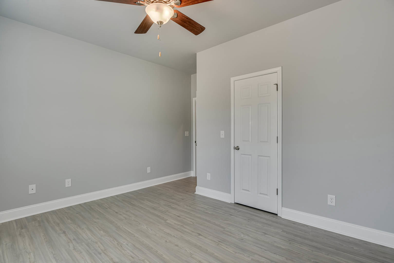 Room with wood laminate flooring, white walls, ceiling fan with light fixture, and white door with silver knob