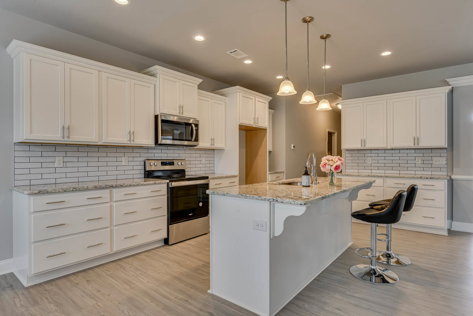 Marble kitchen island with black and silver bar stools, open microwave, stove, white cabinetry, bouquet of pink flowers in glass vase