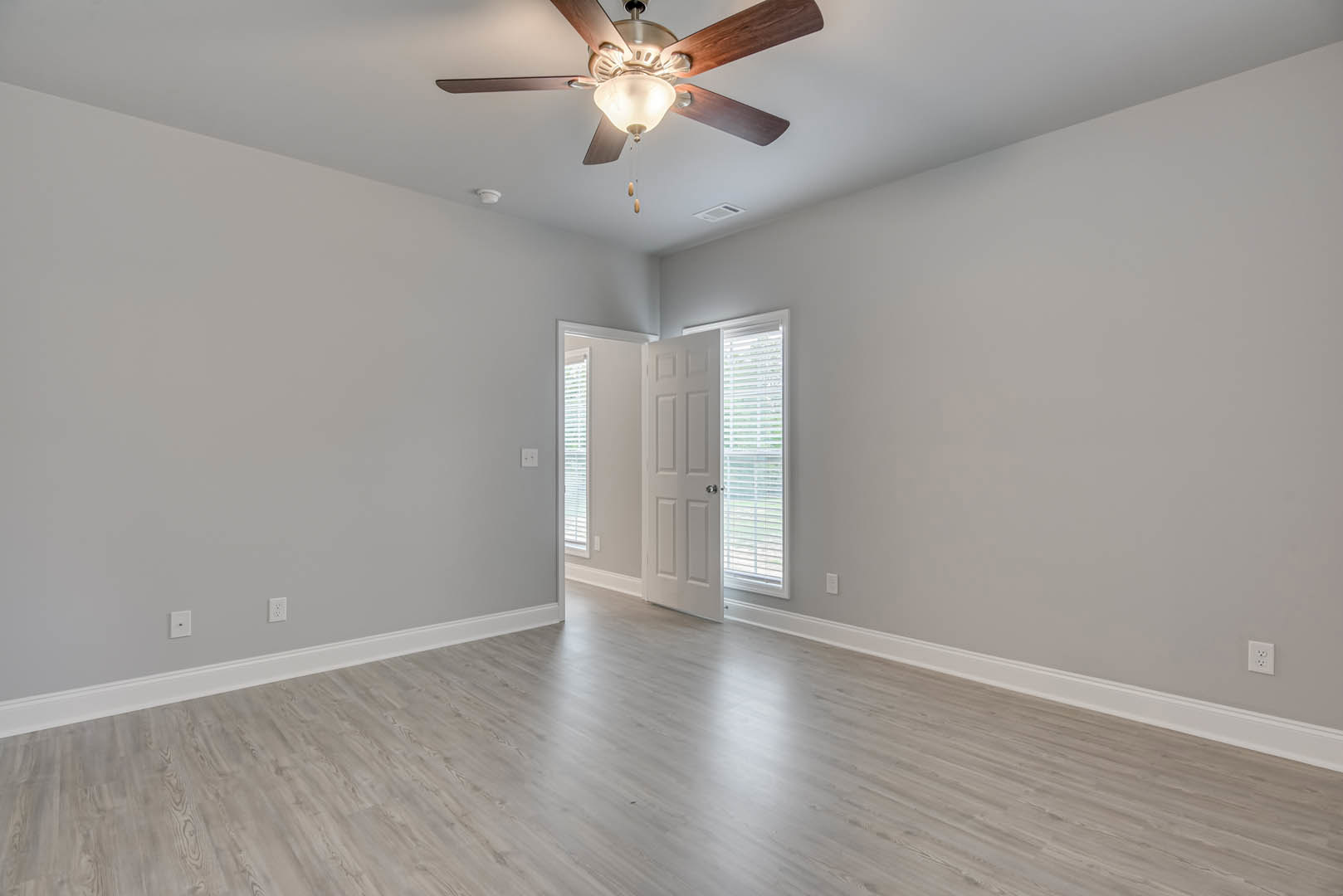 Hardwood floor room with white door, silver knob, ceiling fan with light fixture, window with closed blinds, white walls, and plaster ceiling.