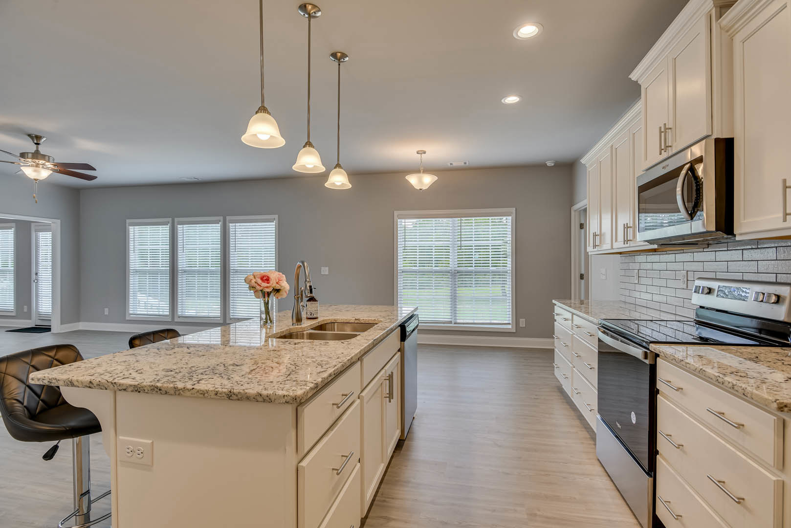 Marble countertop kitchen with stainless steel stove, white cabinetry, window with blinds, glass vase of pink flowers, and upholstered chair with foot pedal