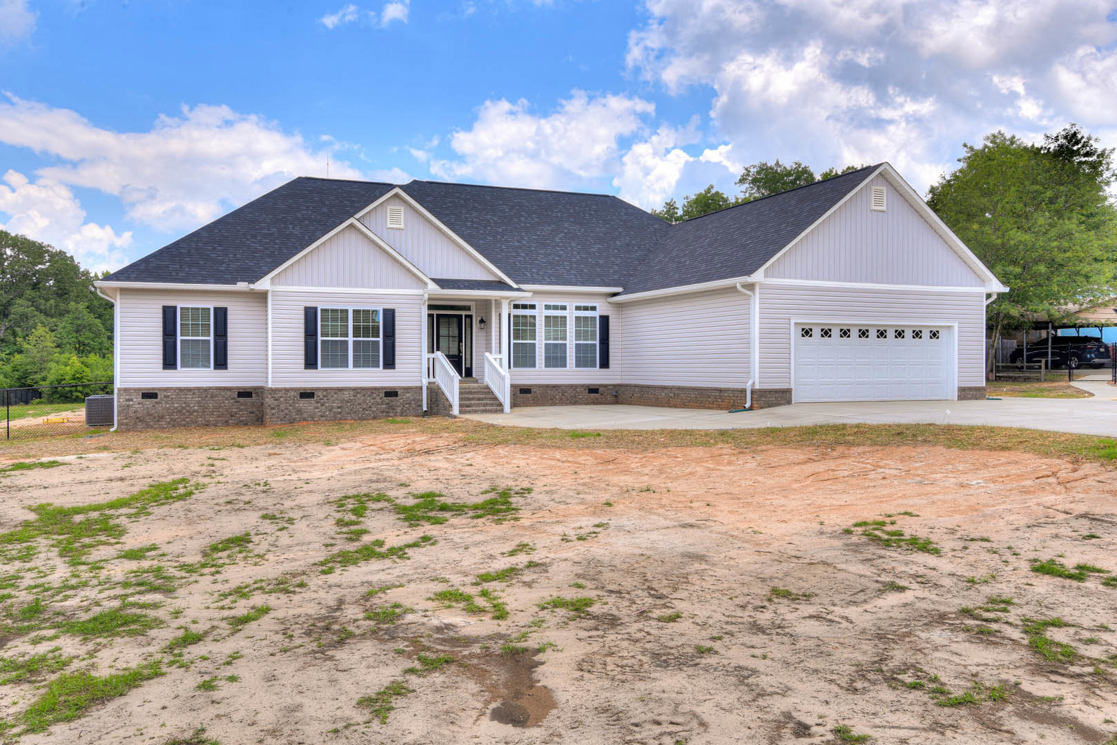Two-story house with white siding, attached garage, concrete driveway, covered front porch with stairs, white-framed windows, and grassy yard under a partly cloudy sky.