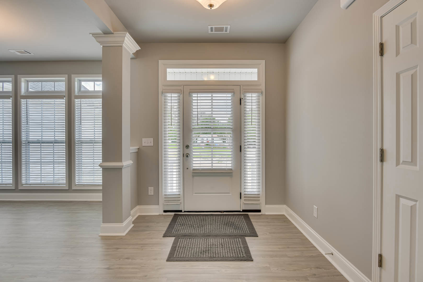 Hallway with white door featuring blinds, two grey rugs on wood laminate flooring, white walls with molding