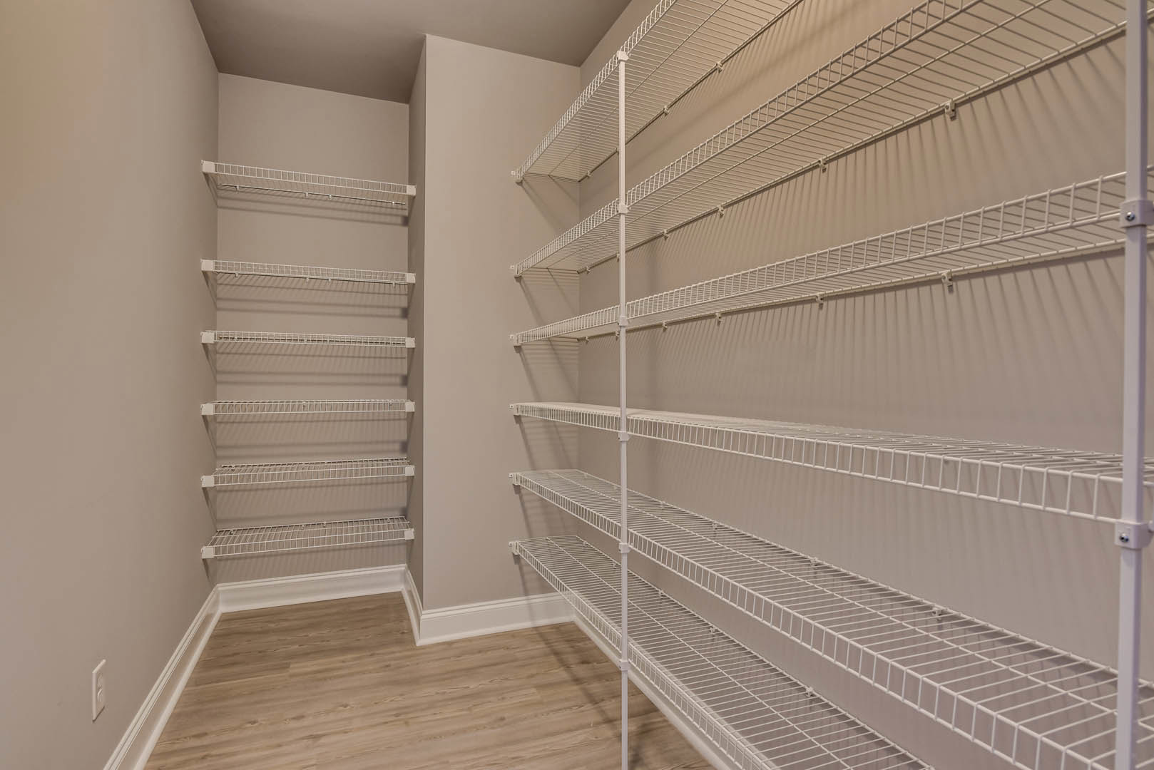 Hardwood floor with white baseboard, white wire shelving mounted on plaster wall in residential room
