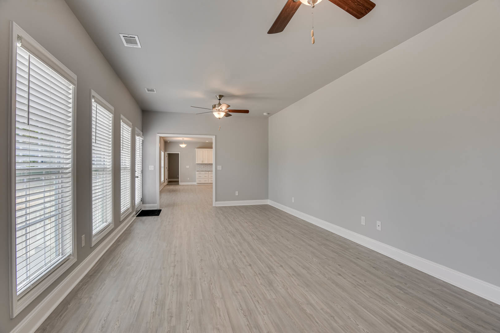 Ceiling fan with light fixture mounted on white plaster ceiling, wood laminate flooring, window with closed blinds, wall vent visible