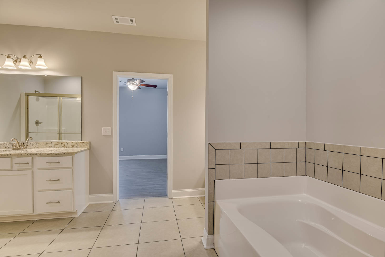 Freestanding white bathtub beside a glass shower enclosure, gray tile flooring, modern sink with chrome faucet, large wall mirror, and recessed lighting