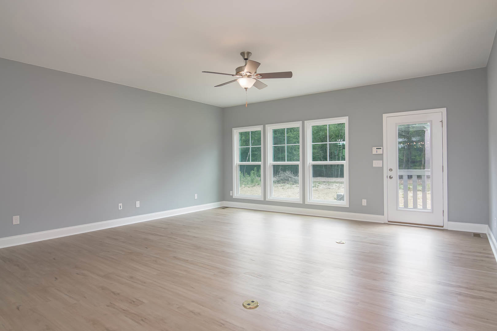Ceiling fan with light fixture above wood laminate flooring, white framed windows along one wall, white door with glass insert, plaster walls with crown molding