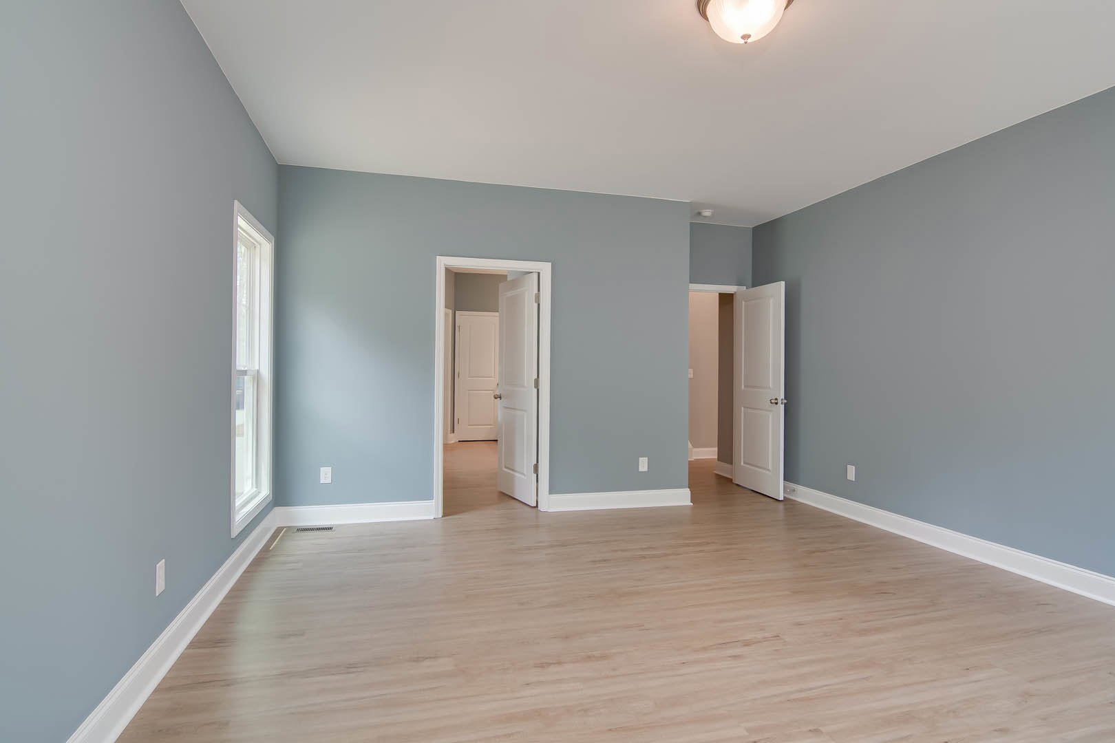 Hardwood floor with light blue plaster wall, white door featuring silver knobs, window, and ceiling light fixture