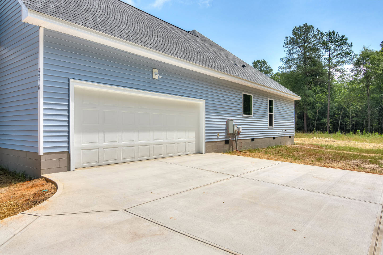 White garage door with blue roof, concrete driveway, light siding, and trees in the background