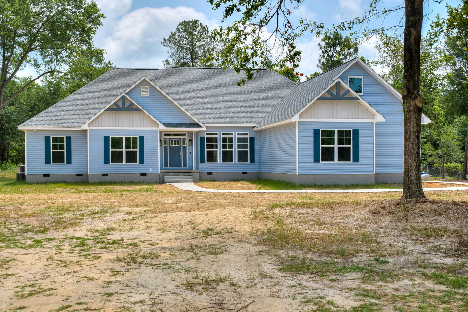 Blue house with white trim, blue front door, dirt yard, and sparse grass; windows set in blue siding under partly cloudy sky.