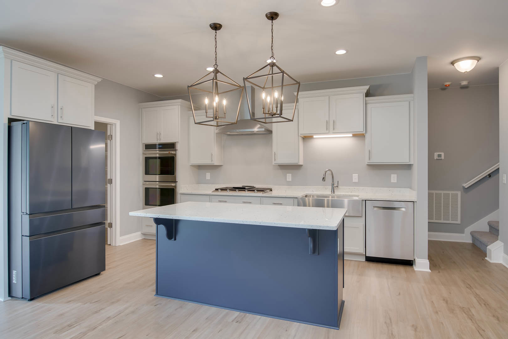 Open-concept kitchen featuring a blue and white island countertop, stainless steel refrigerator, dishwasher, and microwave, white cabinetry with black-framed door, light walls, and