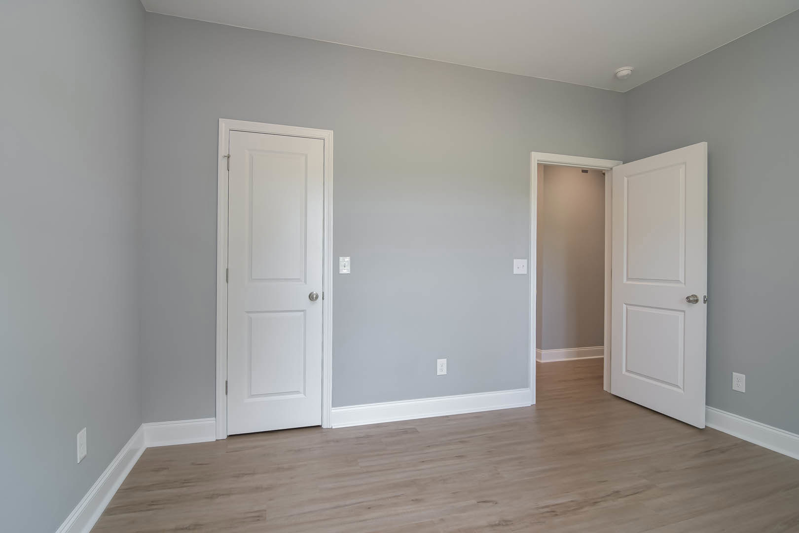 Wood floor with white baseboards, two white doors with silver knobs, white walls, and ceiling in a residential interior.