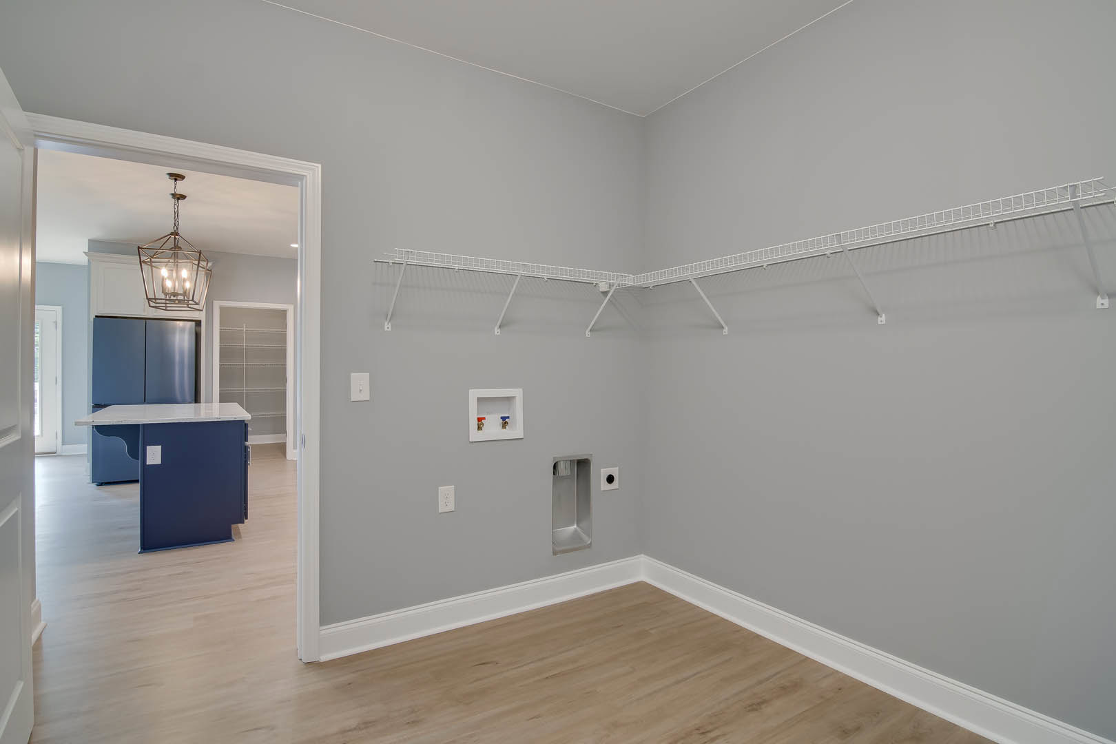 Open-concept kitchen with blue cabinetry, wood flooring, white walls, pendant light fixture, and a white island featuring two faucets and a black handle.