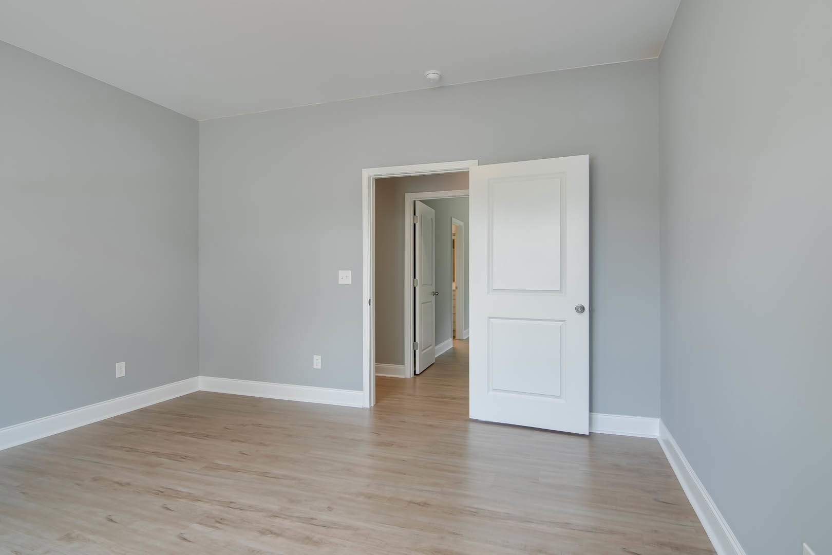 White paneled door with silver handle open to room with light wood laminate flooring, white walls, and white cabinet visible in foreground.