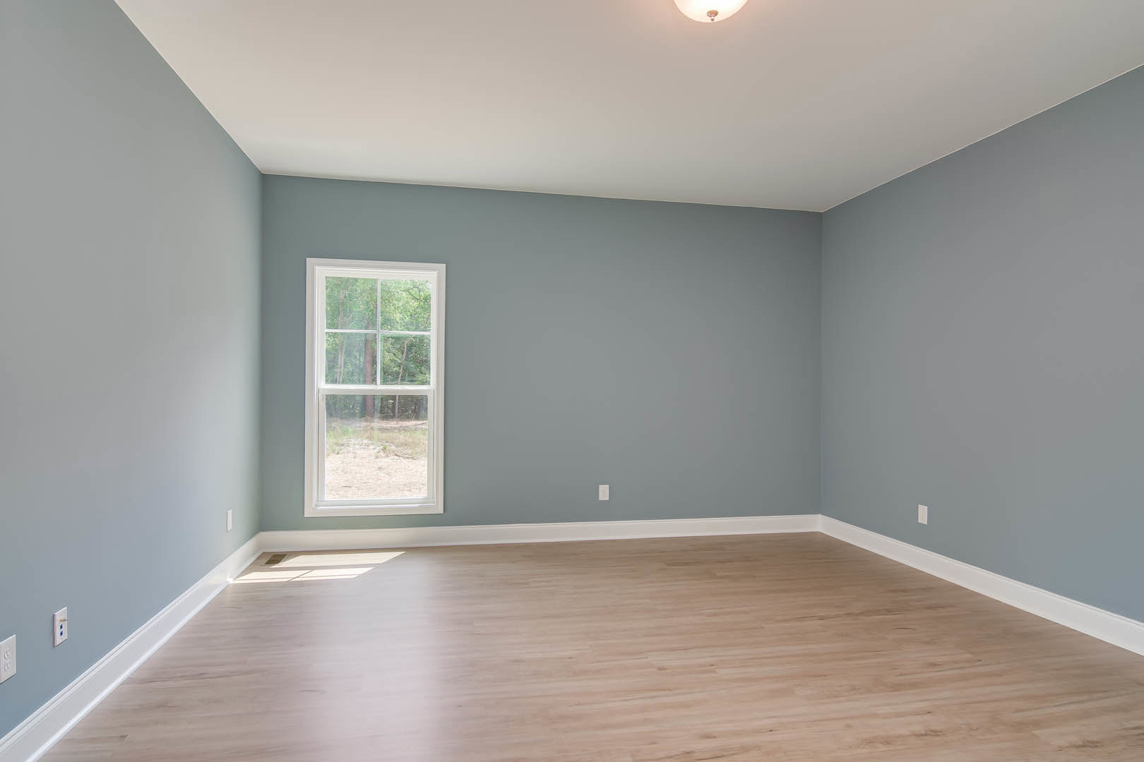 Hardwood floor with white baseboard trim, large window overlooking forested landscape, white plaster walls, white ceiling with recessed light fixture