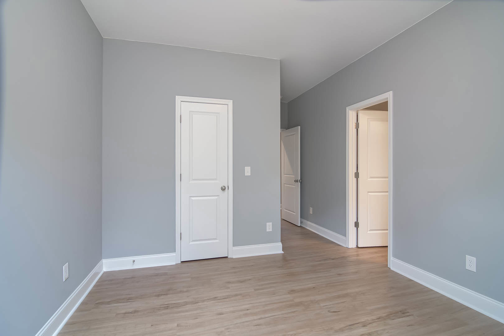White paneled doors with silver knobs, hardwood floors, white baseboards, and smooth white walls in a residential interior.