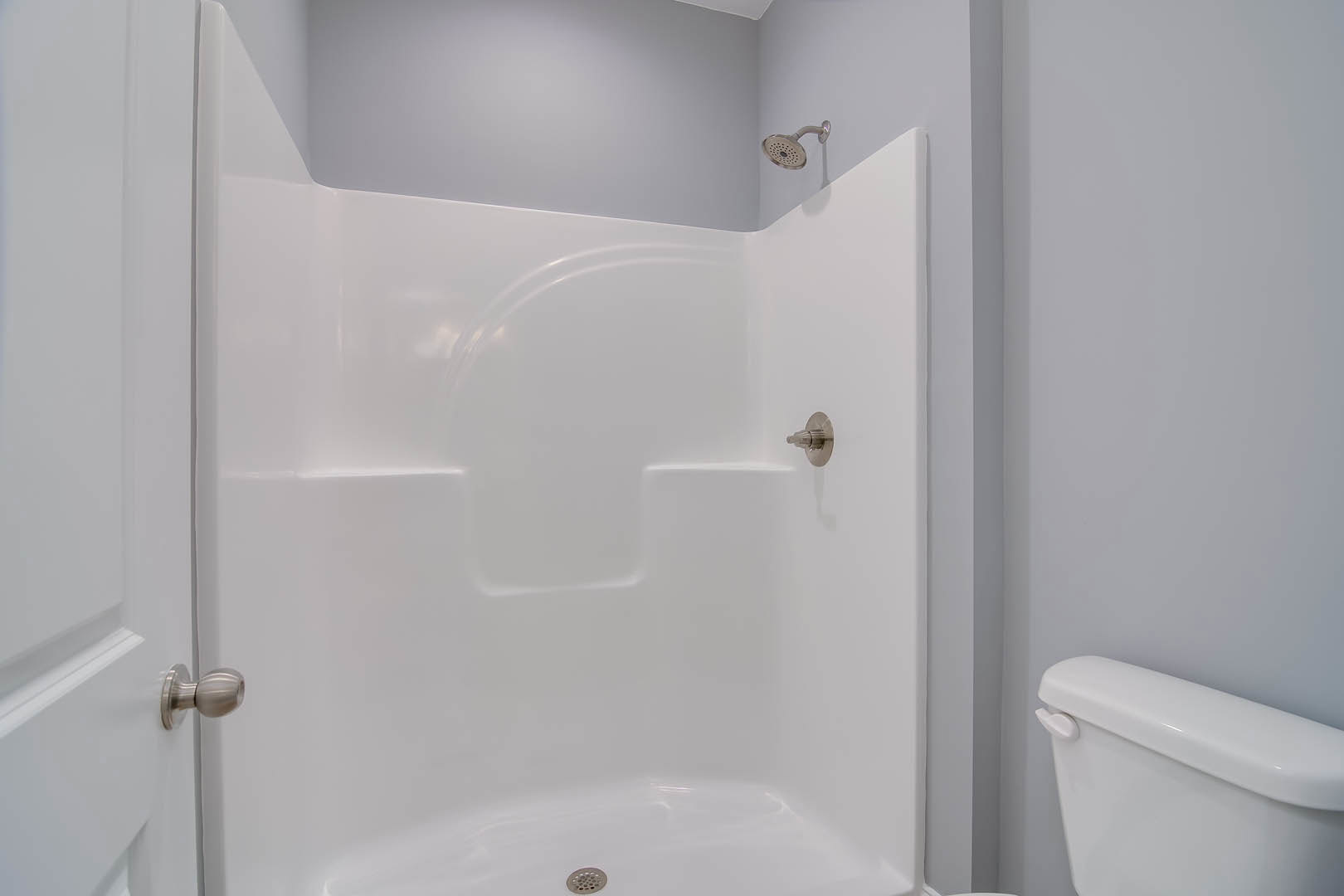 White tile shower with chrome showerhead next to a white toilet and metal door handle in a modern bathroom.