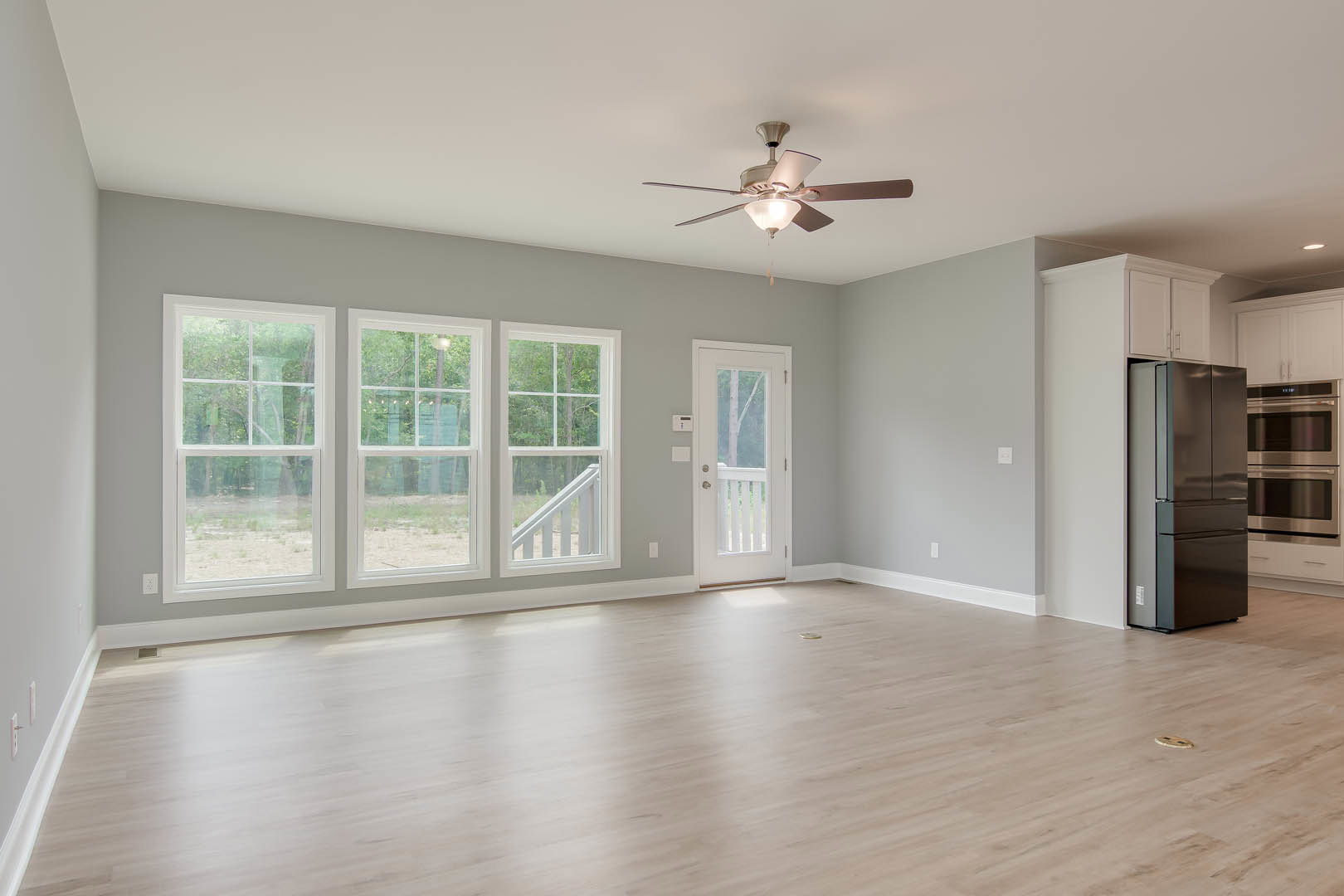 Hardwood floor room with ceiling fan, row of windows with white trim, white door with glass panel, stainless steel refrigerator and microwave