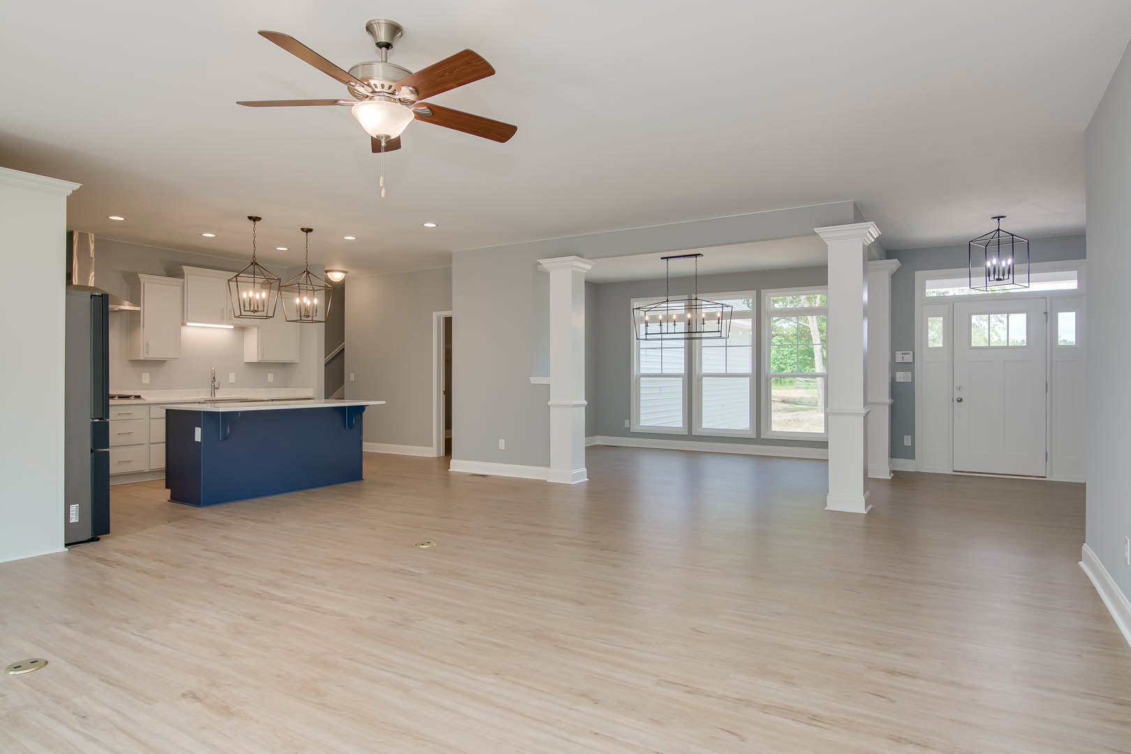 Spacious open floor plan featuring hardwood flooring, blue accent wall with white countertop, kitchen and dining area, ceiling fan with light, chandelier, and white door with glass
