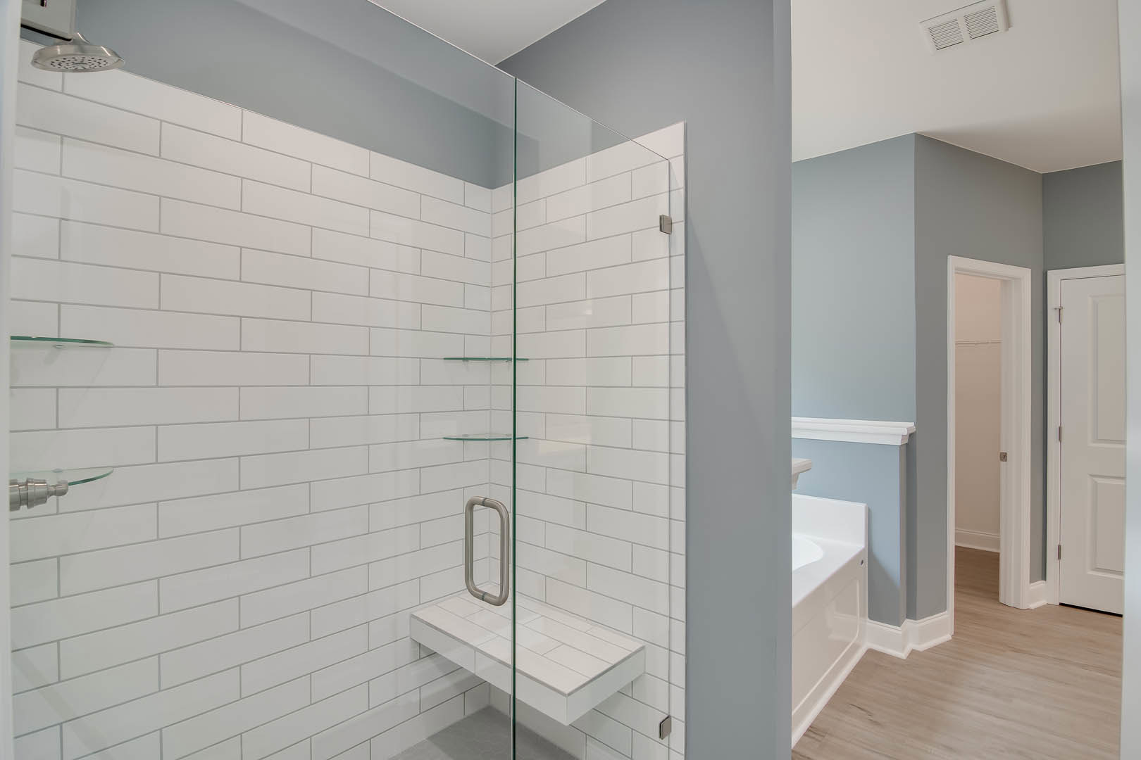 Bathroom featuring a frameless glass shower enclosure, white tile walls, built-in bathtub, and silver metal fixtures