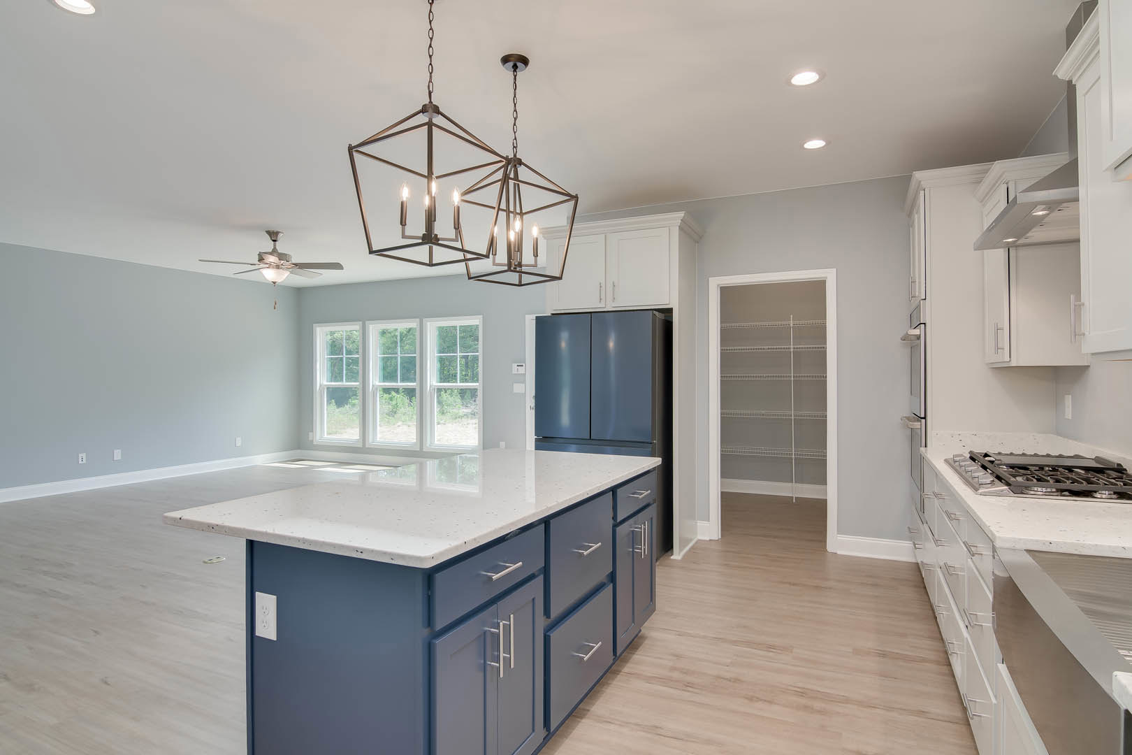 Spacious kitchen featuring a marble-topped island, ceiling fan, white cabinetry, stainless sink, and a row of windows providing natural light