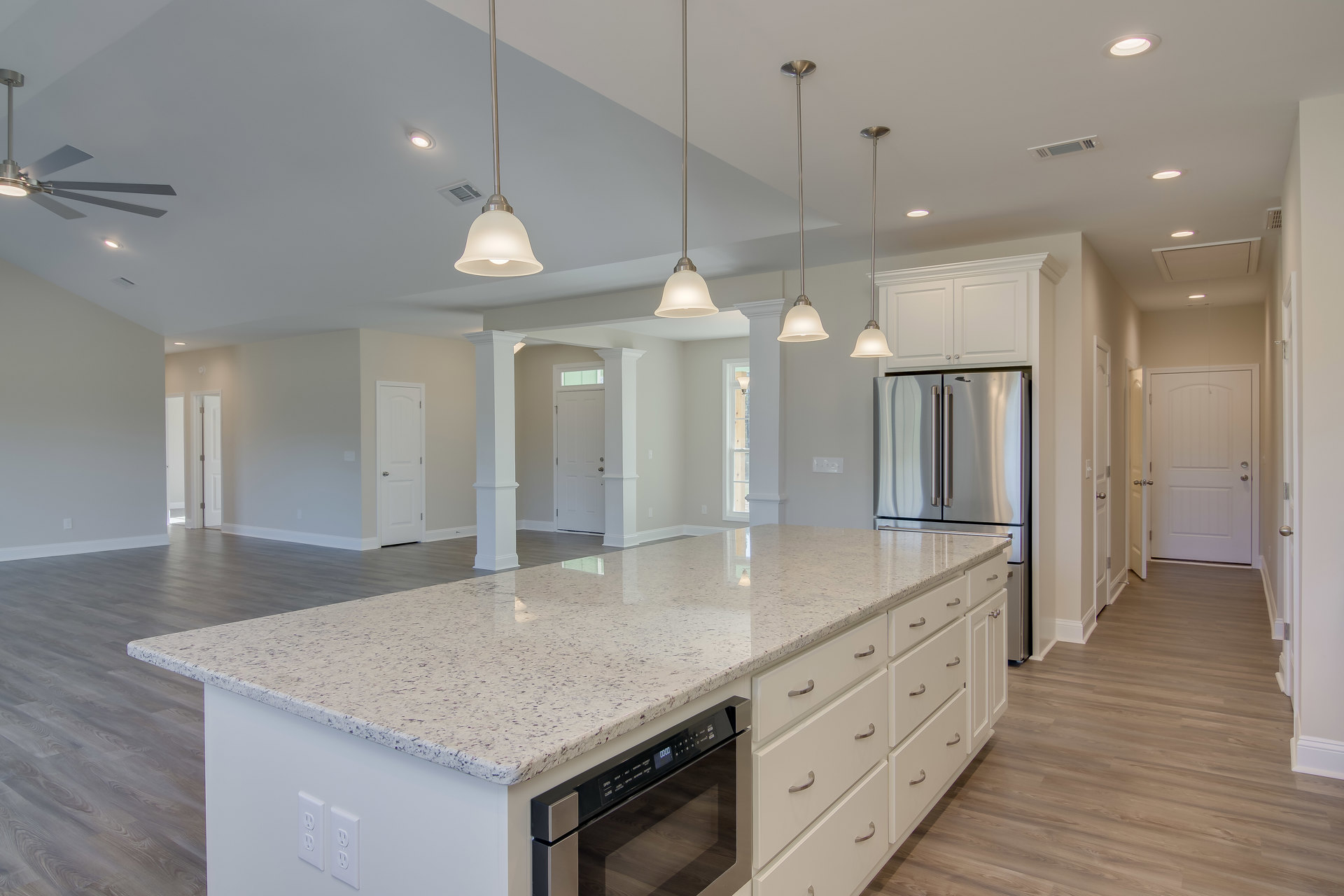 Spacious kitchen featuring a large central island with built-in microwave, white cabinetry, tile flooring, stainless steel fixtures, and a white door with silver knobs