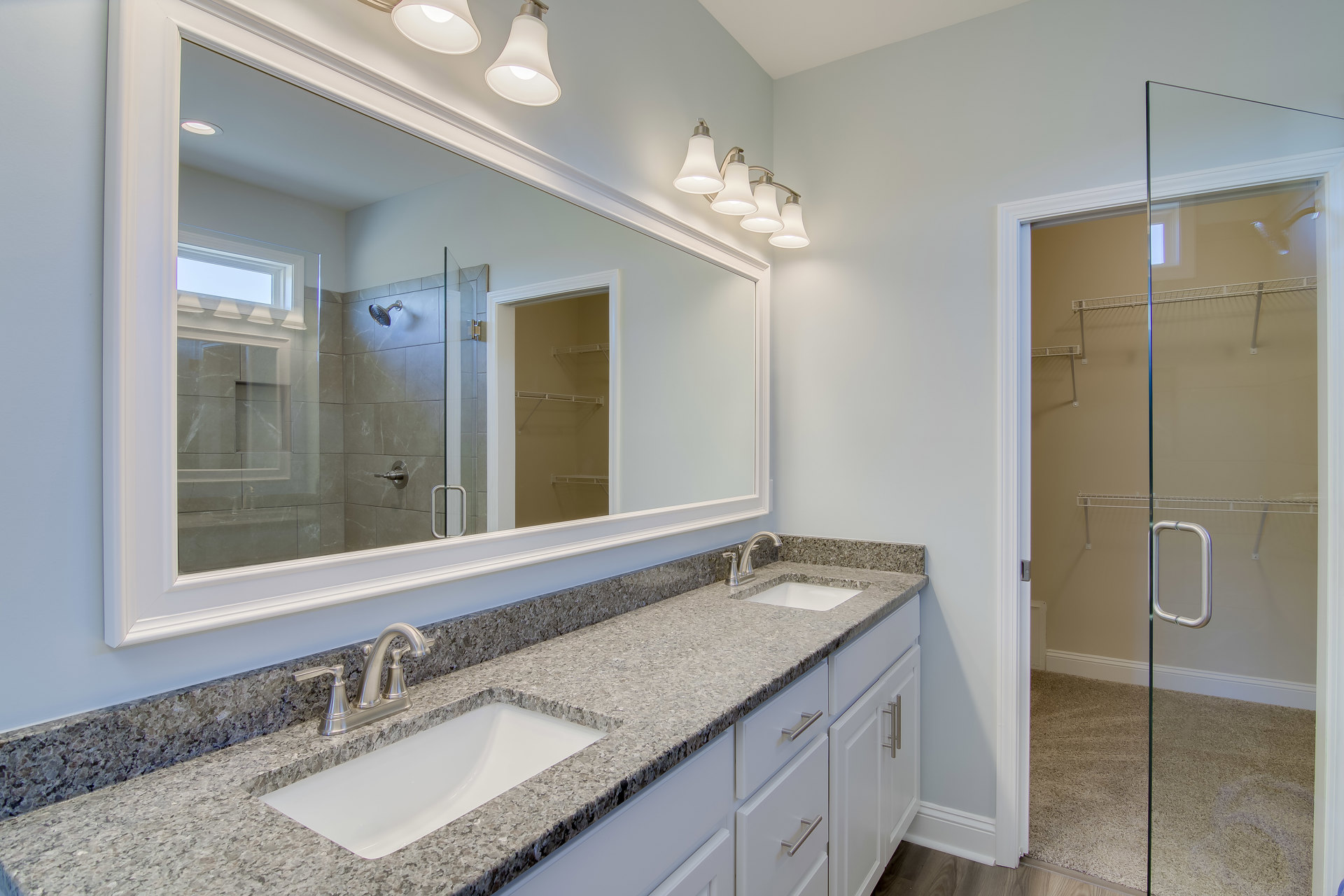 Double vanity with undermount sinks, chrome faucets, expansive wall mirror, quartz countertop, and modern light fixtures above, set against neutral tile backsplash in a