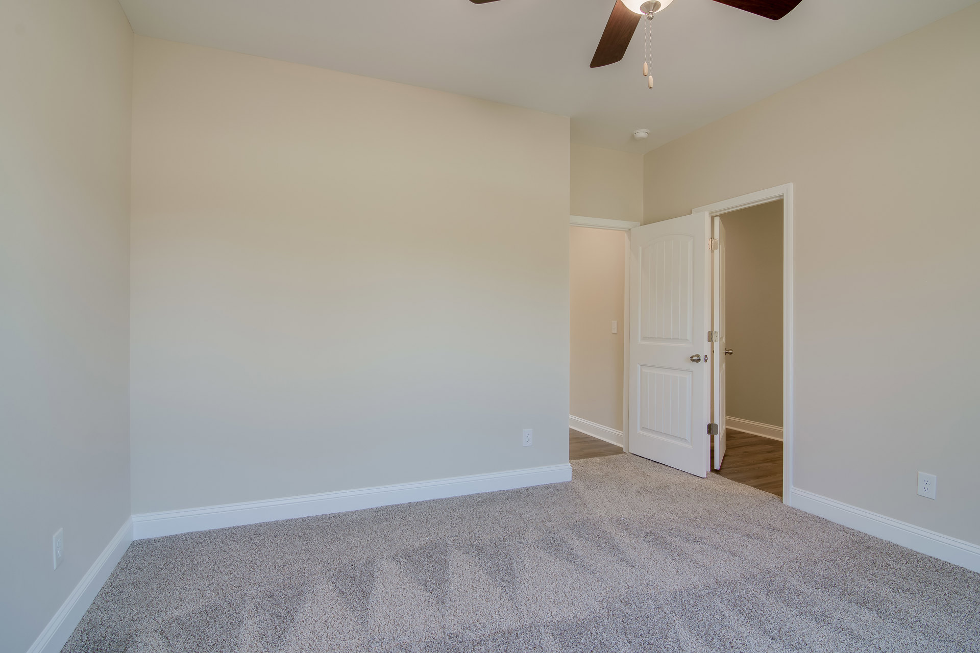 Carpeted room with white walls, ceiling fan with light fixture, white door featuring silver doorknob, crown molding along ceiling edges