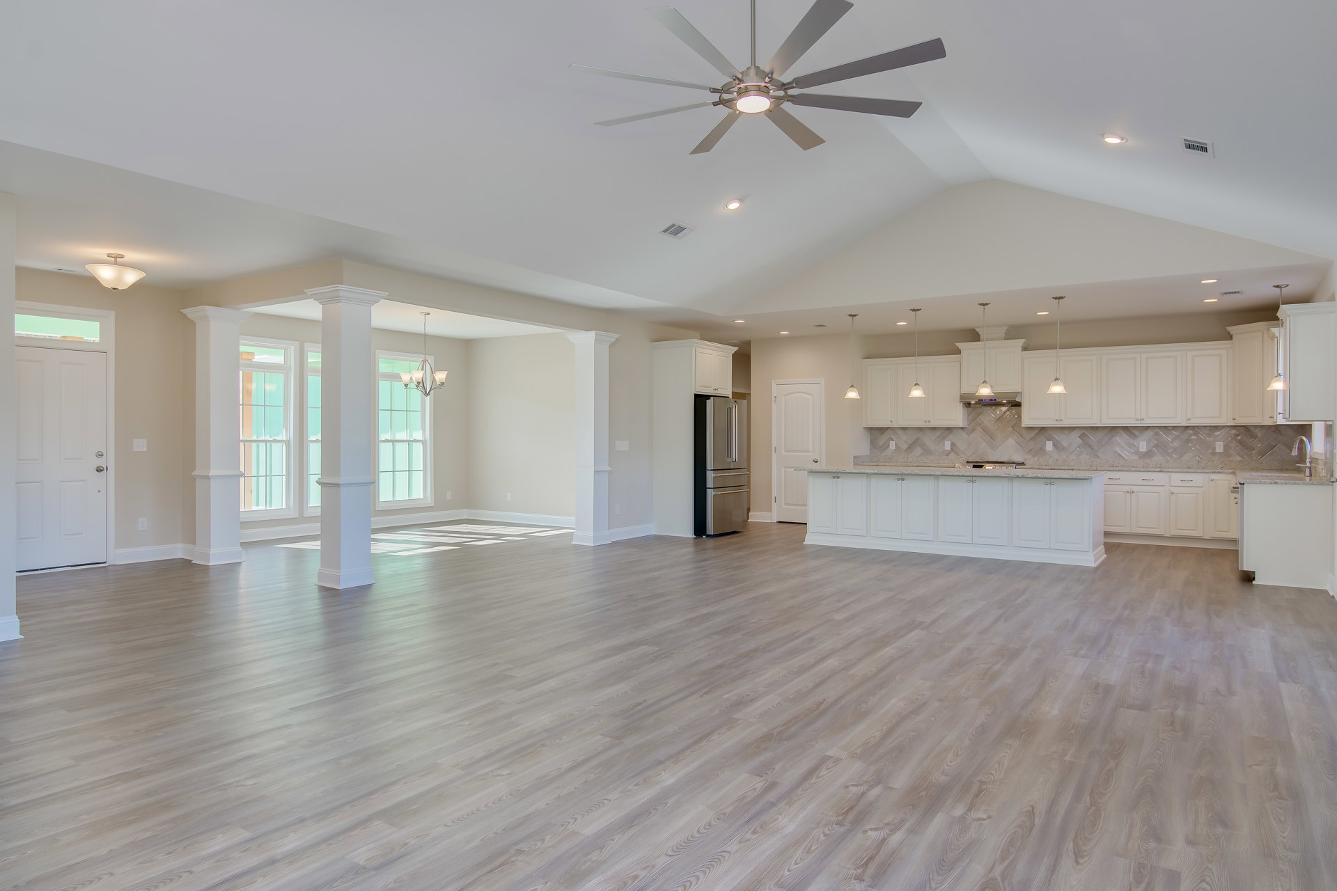 Spacious open floor plan featuring laminate flooring, white kitchen cabinets with marble countertops, stainless steel refrigerator, stove, ceiling fan with light fixture, and