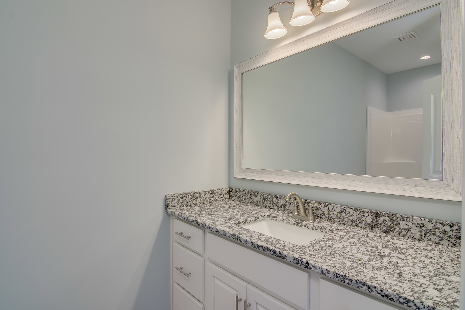 Bathroom featuring a marble countertop with undermount sink, large framed mirror above, white bathtub with silver faucet, and ceiling-mounted light fixture.